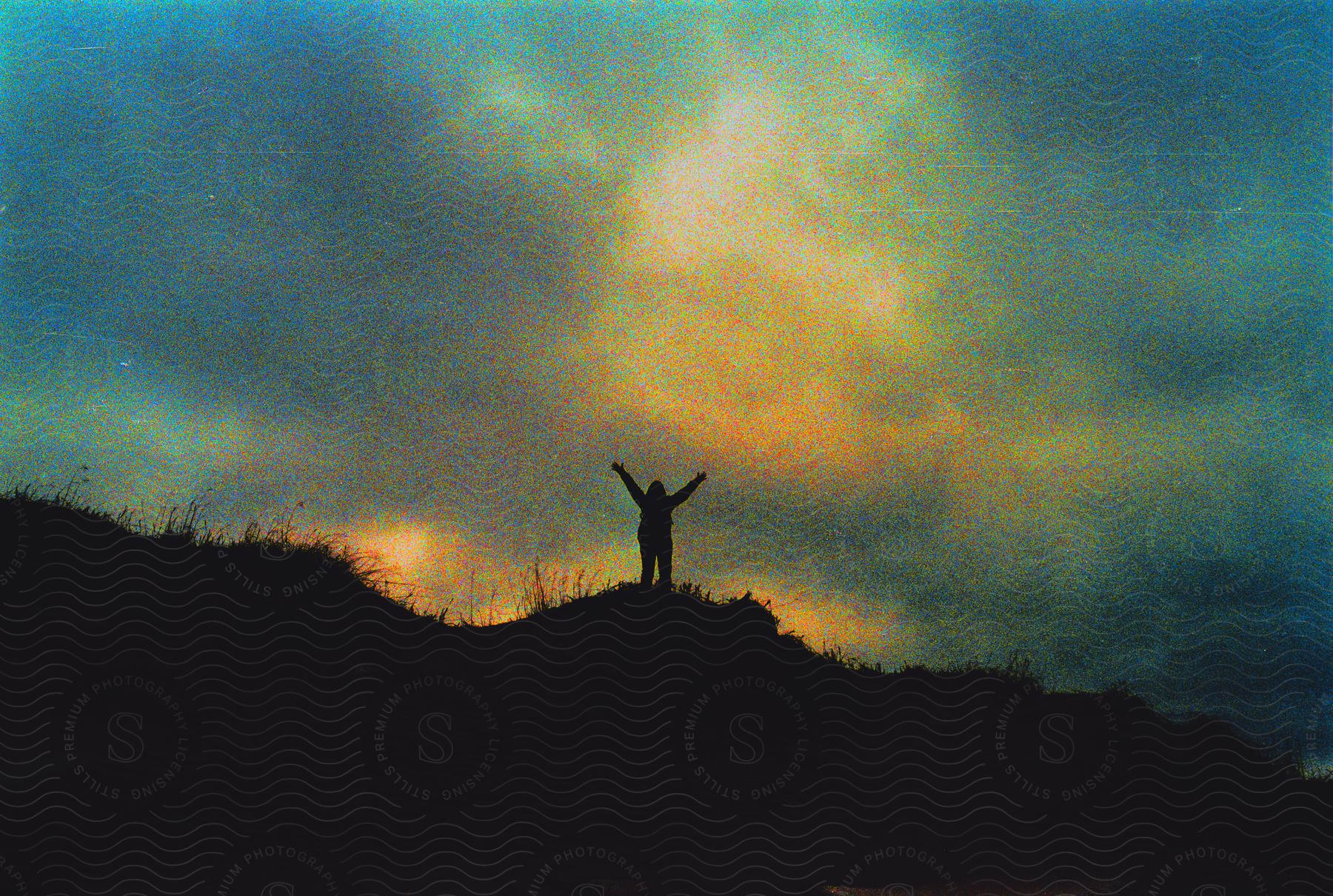 Silhouette of a person with arms up on top of a peak.