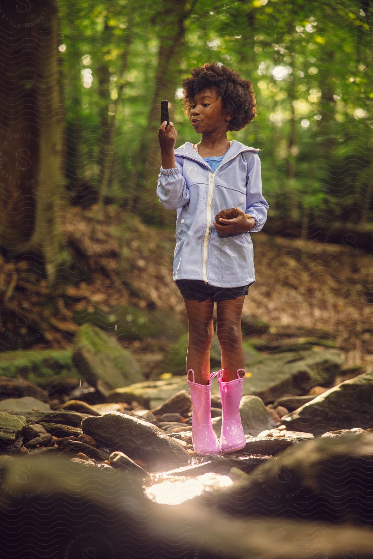 Stock photo of a girl is standing in the woods holding a rock in one hand and her phone in the other hand