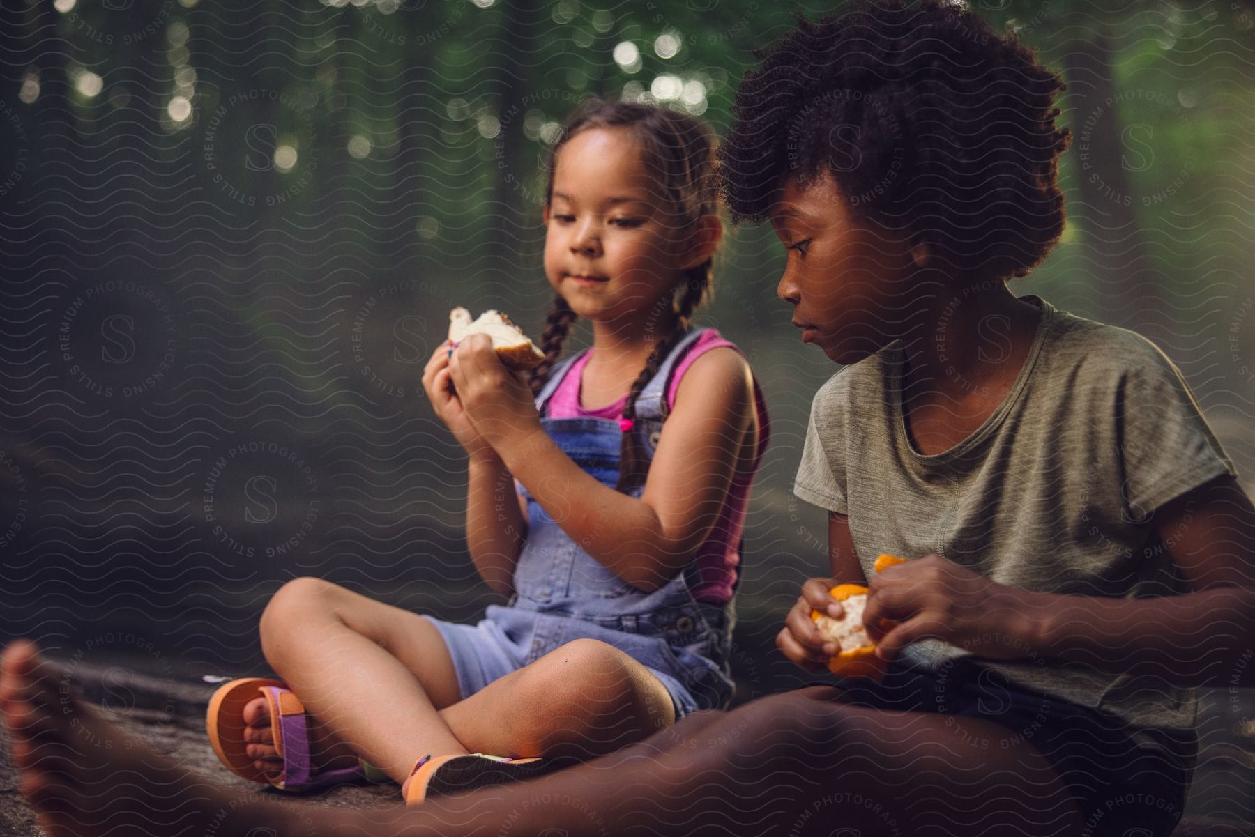 two girls sitting at a forest eating fruit during day time