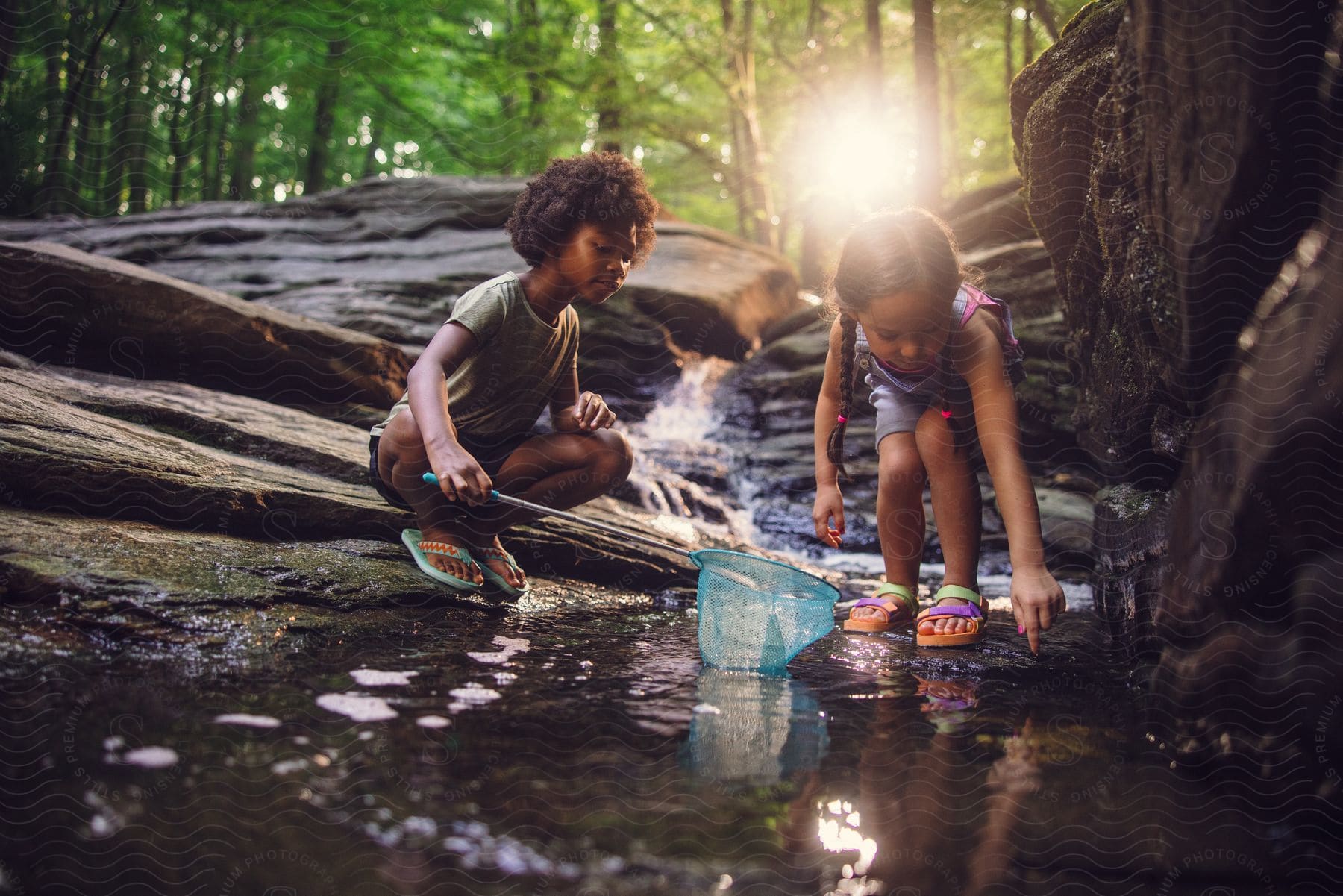 Two young girls bend in a stream and catch fish with a blue net.