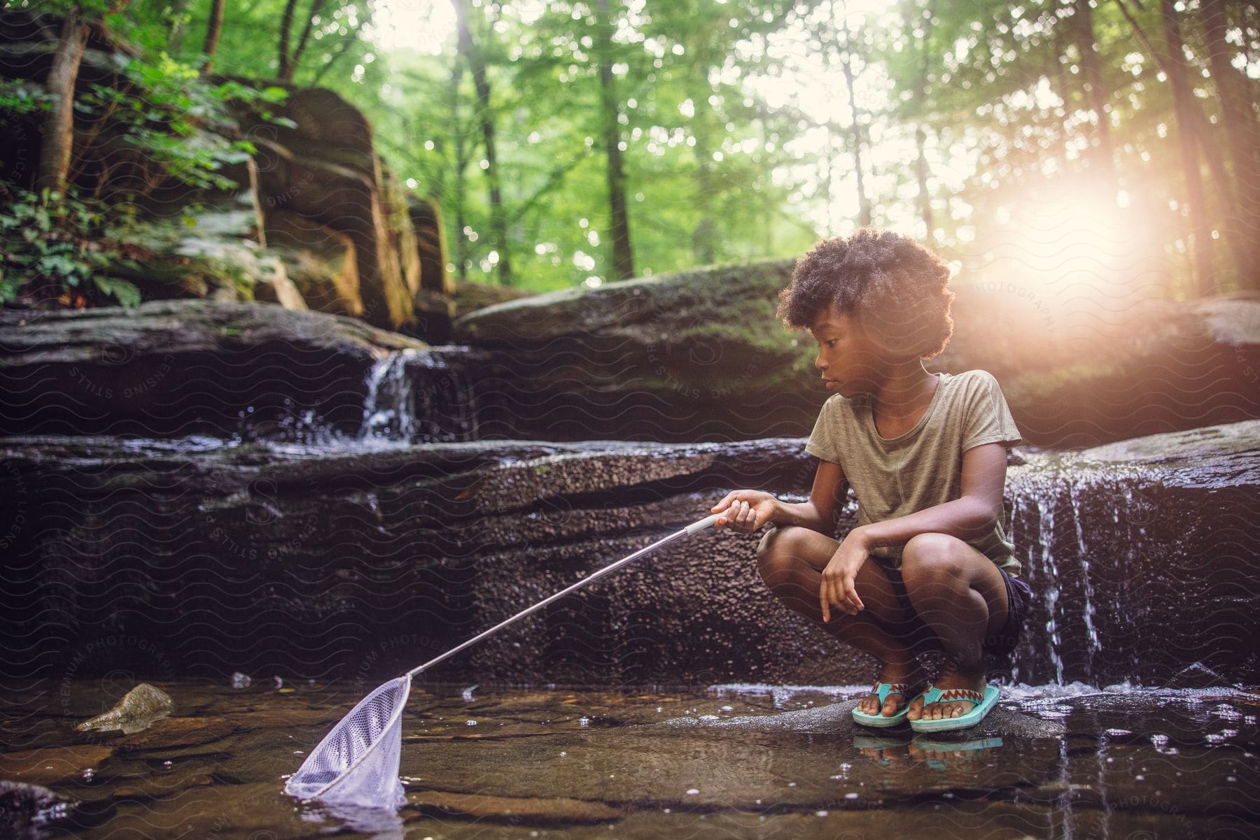 A young African American girl is playing in the woods in a creek.