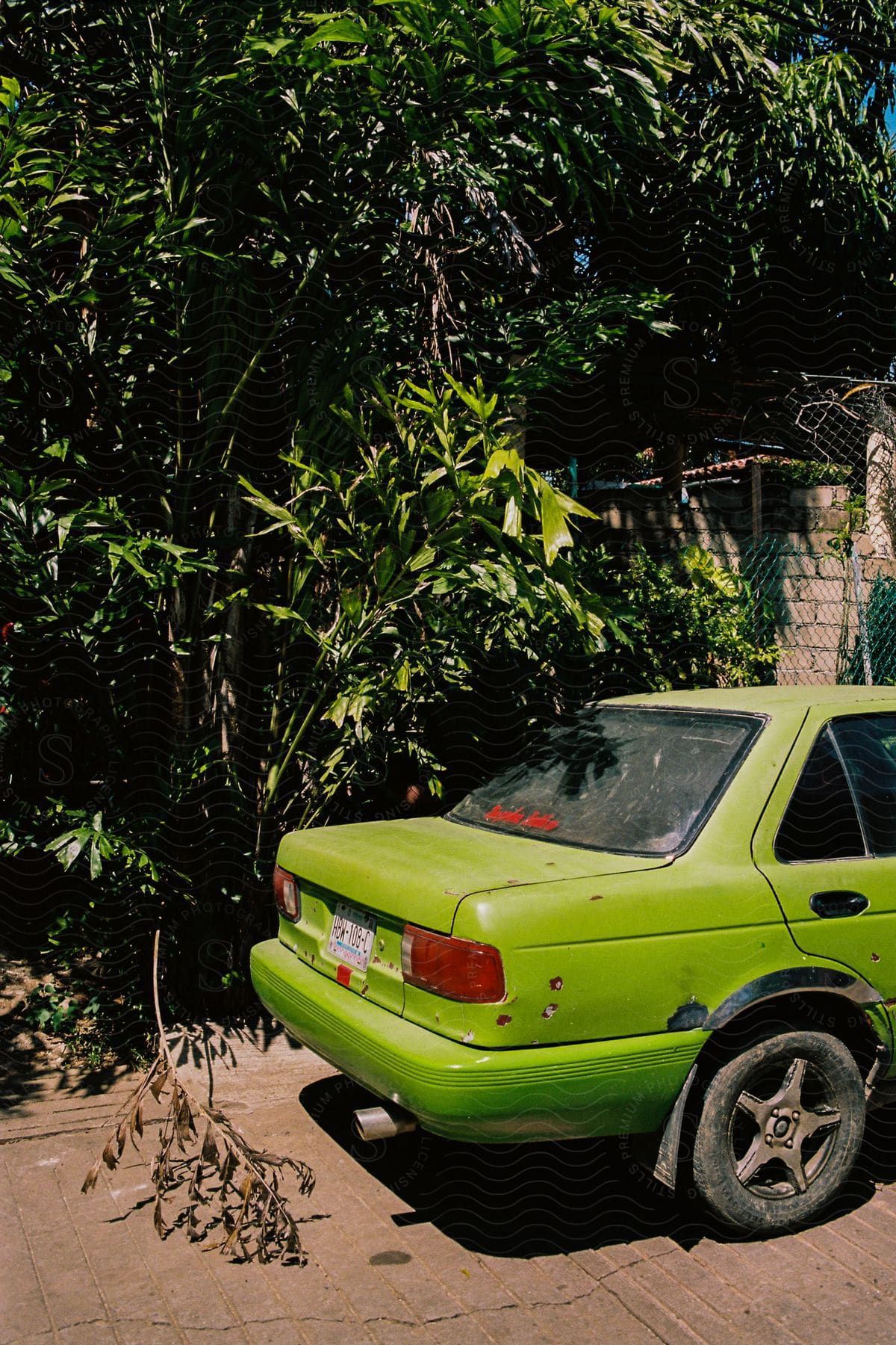 The back end of a light green sedan is shown parked in a driveway on a sunny day.