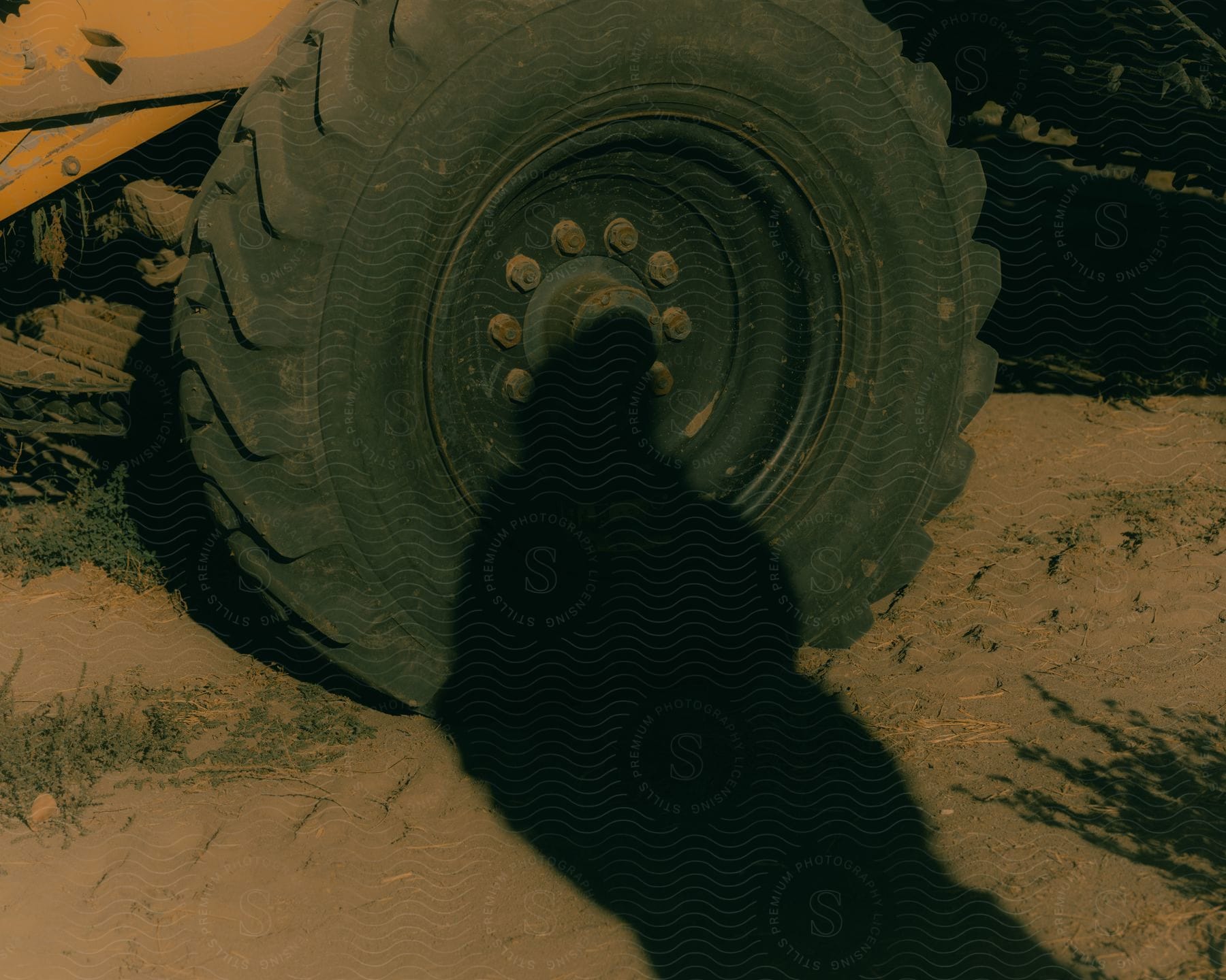 A person's shadow falling on a tractor's tire.