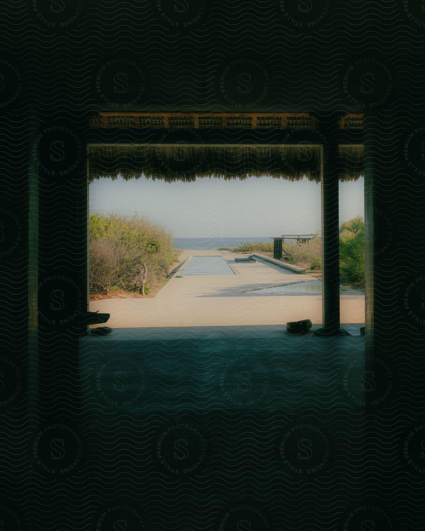 A thatched-roof building with a walkway to the beach overlooks a pool.