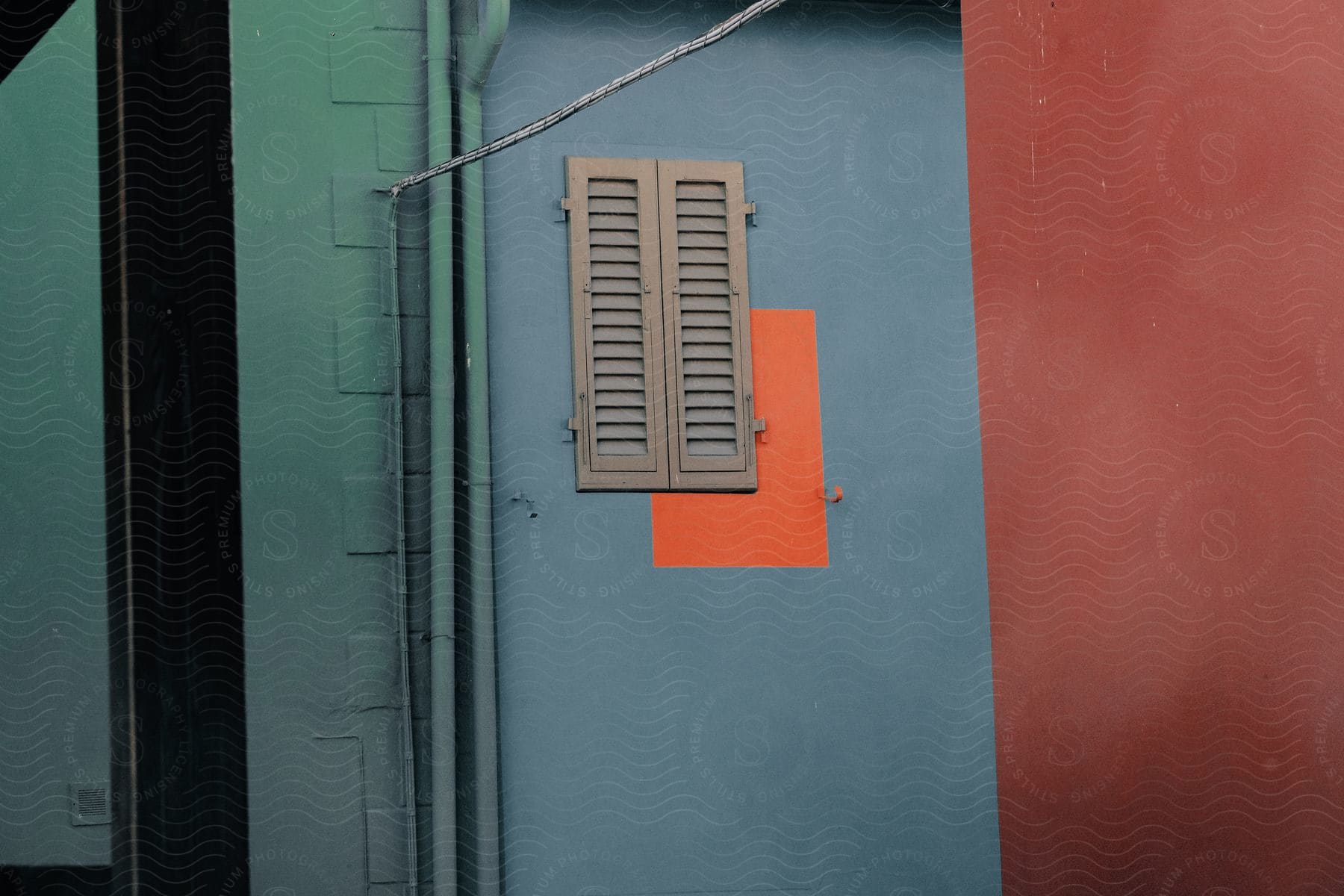 A wooden window shutter on a blue wall, slightly off from the orange rectangle where the window should be.