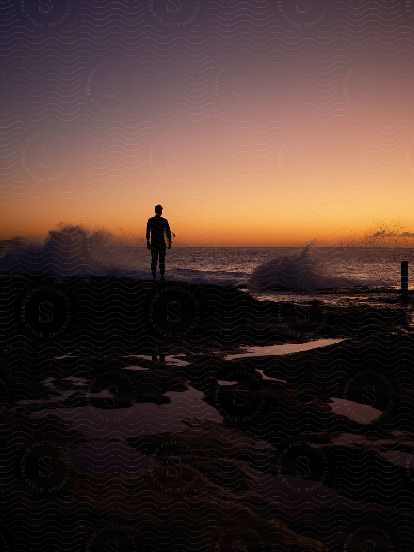 A surfer watching on shore as waves crash into the beach.