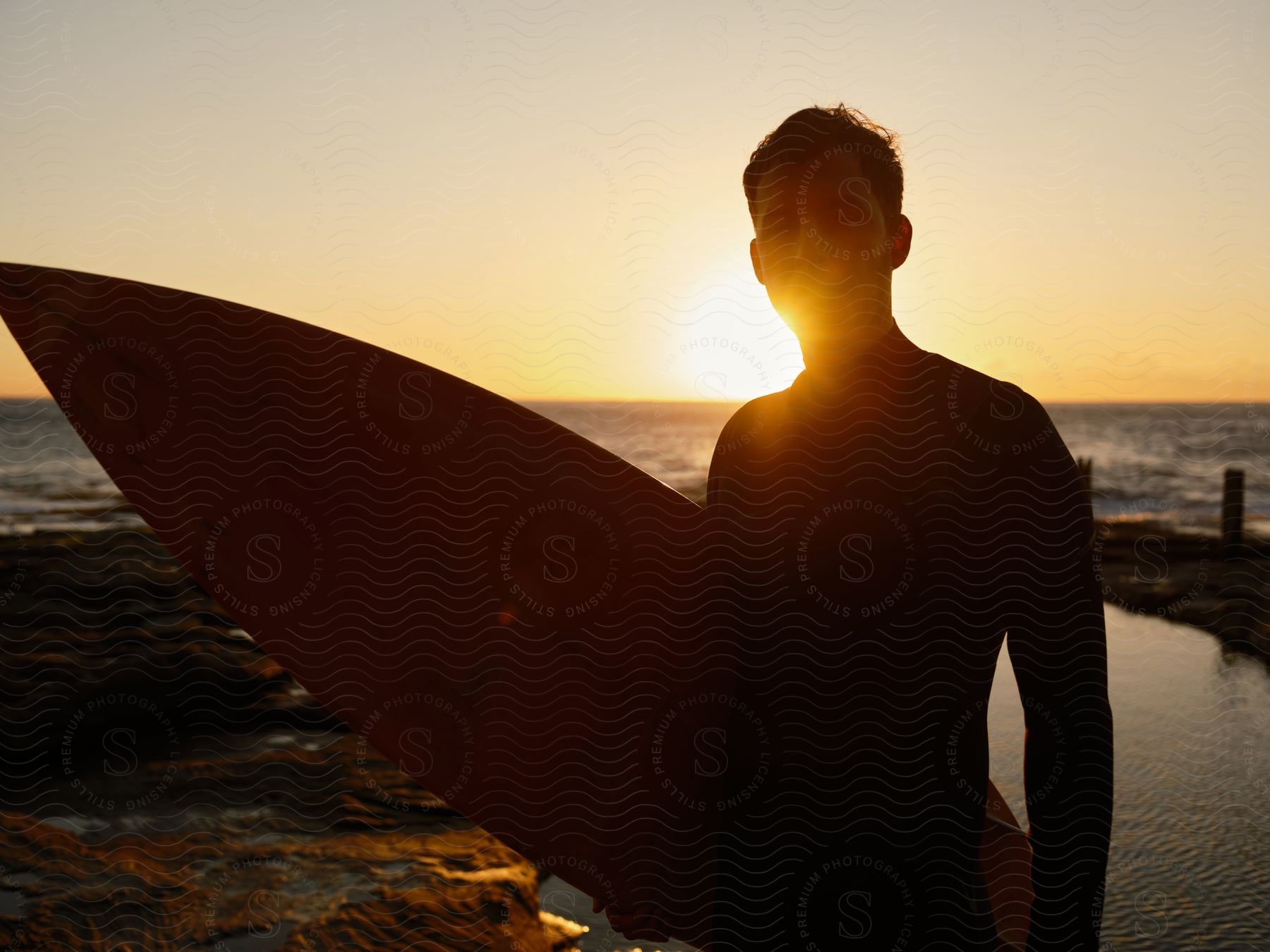 Surfer in wet suit holds surfboard on the beach at sunset