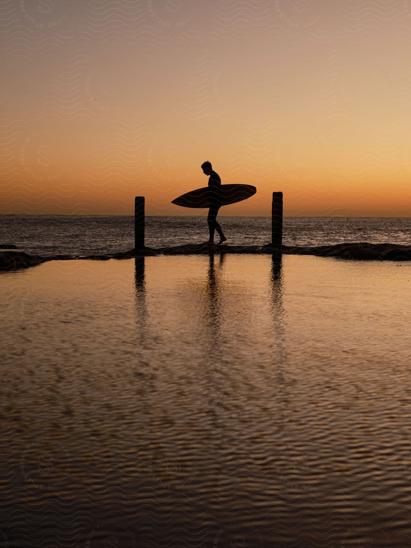 Man walking on the beach with a surfboard under his arm at sunset.