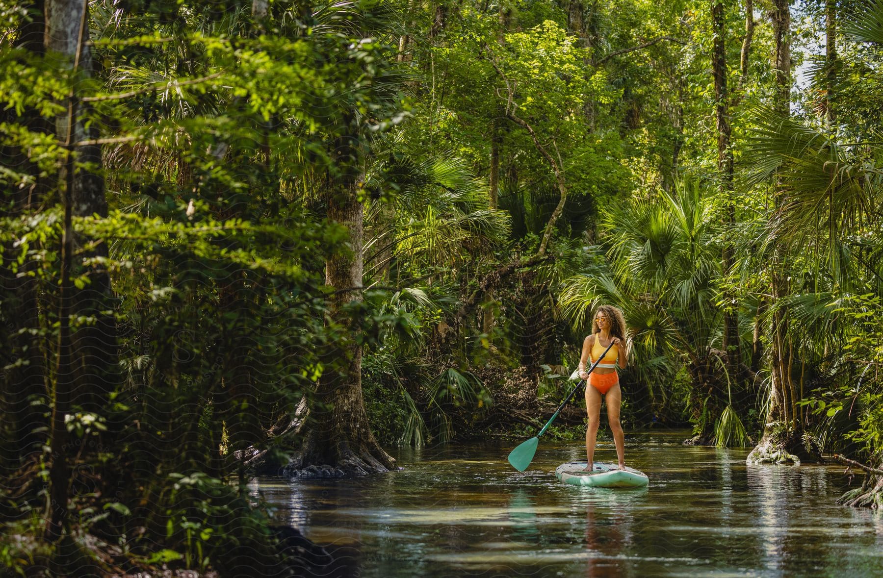 a woman stands on a surfboard and paddles down a river in a jungle