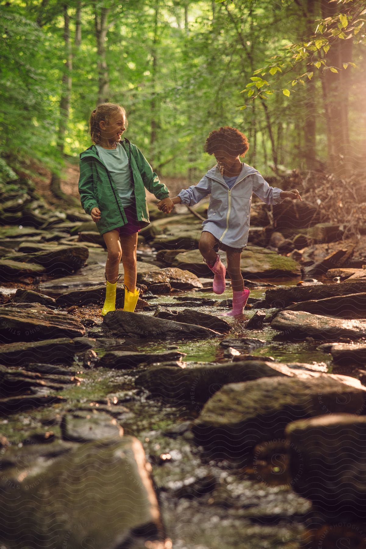 Two girls are wearing rain boots playing in creek in the woods.