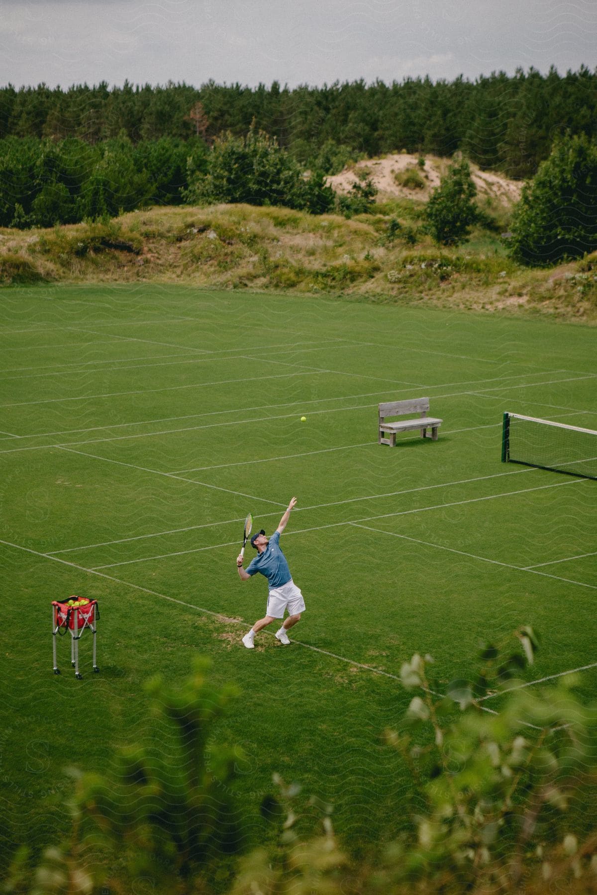 A tennis player holds his racket in the air as the ball flies above his head