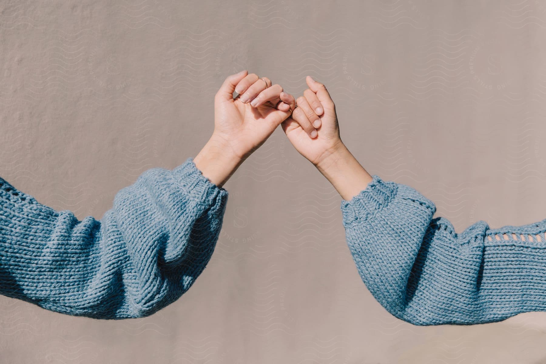 Two people wearing similarly detailed sweaters hook pinkies together.