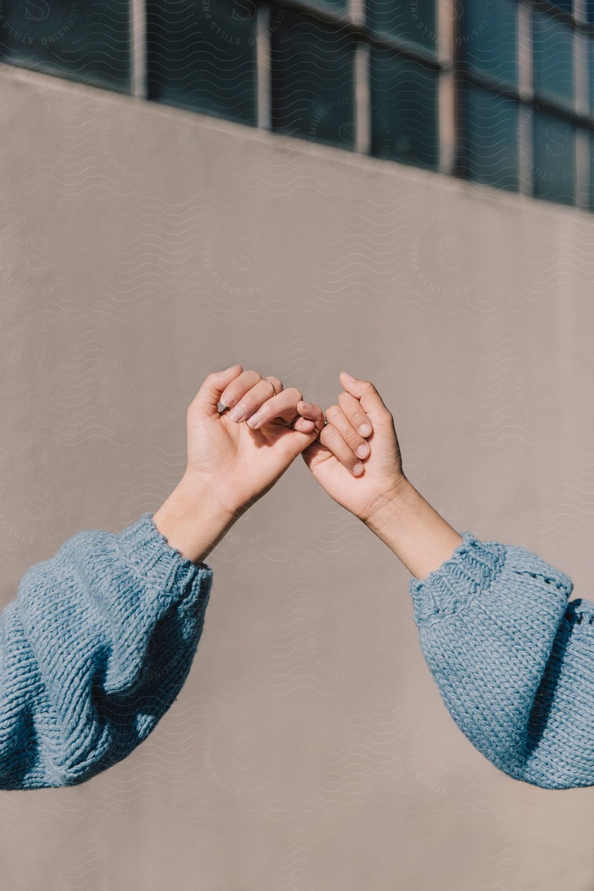 Fingers intertwined with the wall of glass windows in the background.