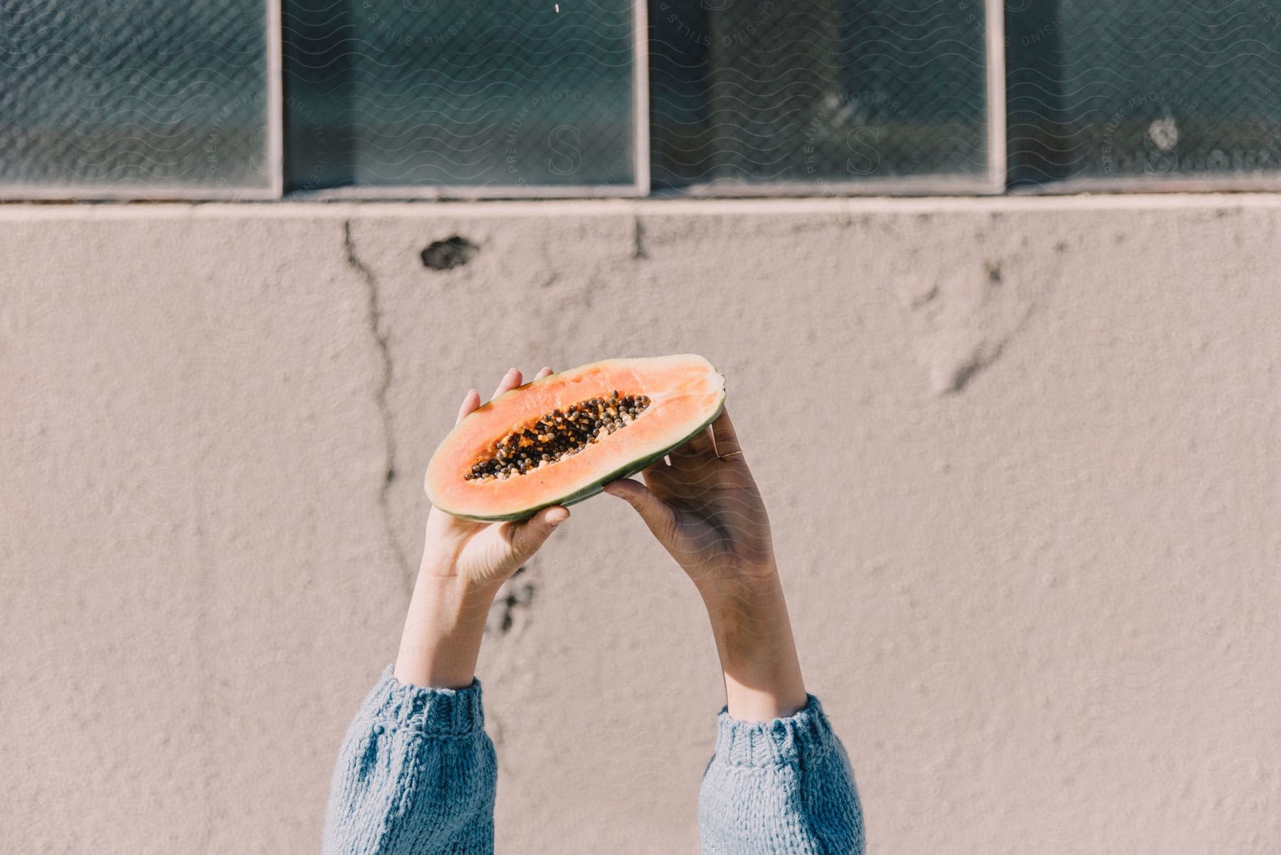 Woman wearing light blue sweater holds up half papaya