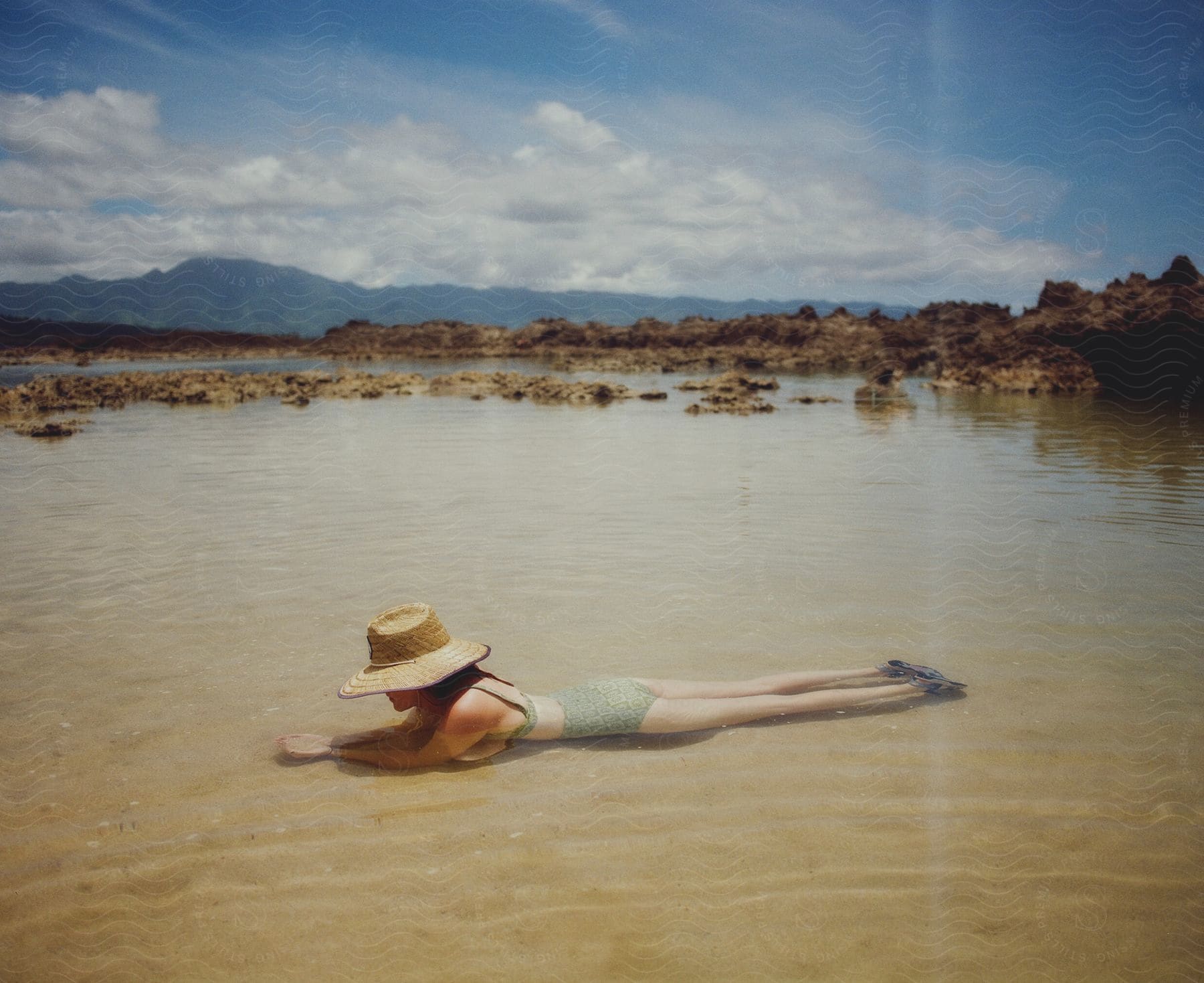 Woman with sun hat and bikini lies face down in water near the beach