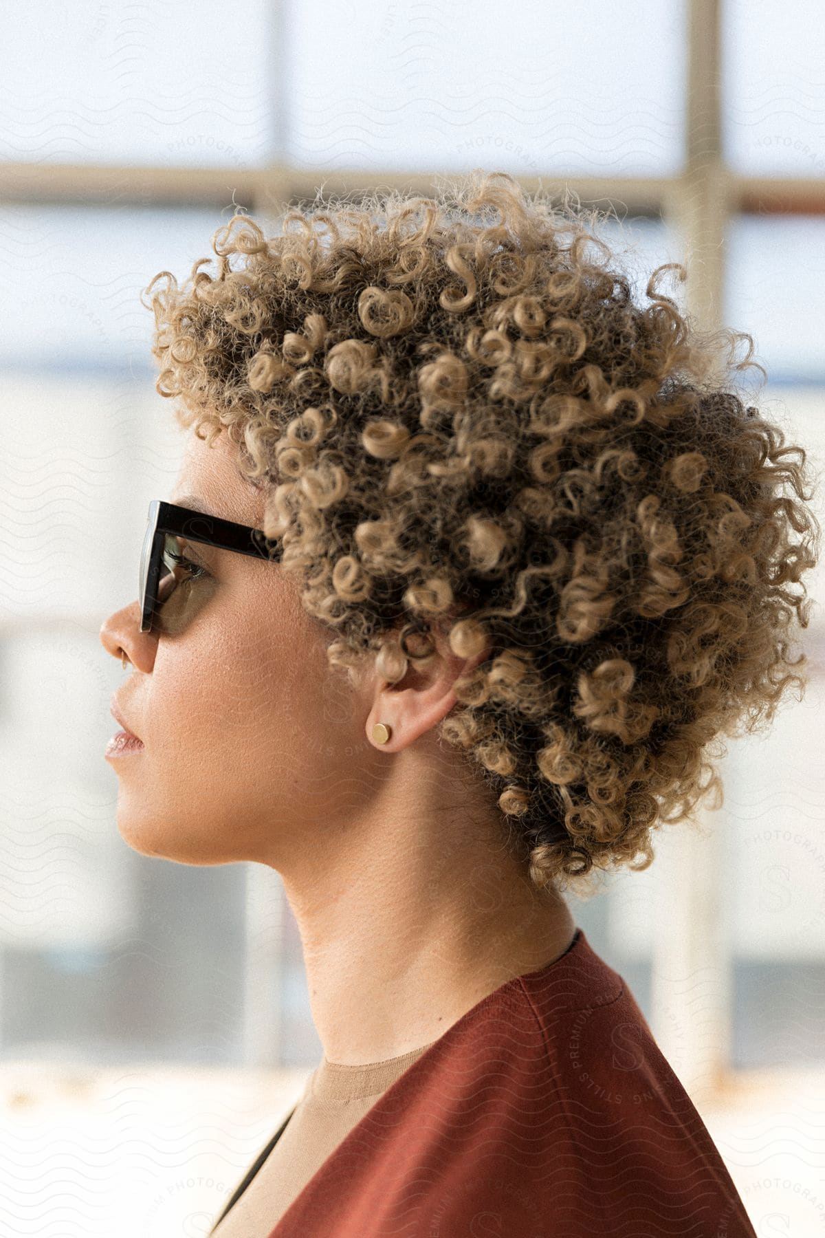 A biracial woman with curly blonde hair poses while wearing sunglasses.