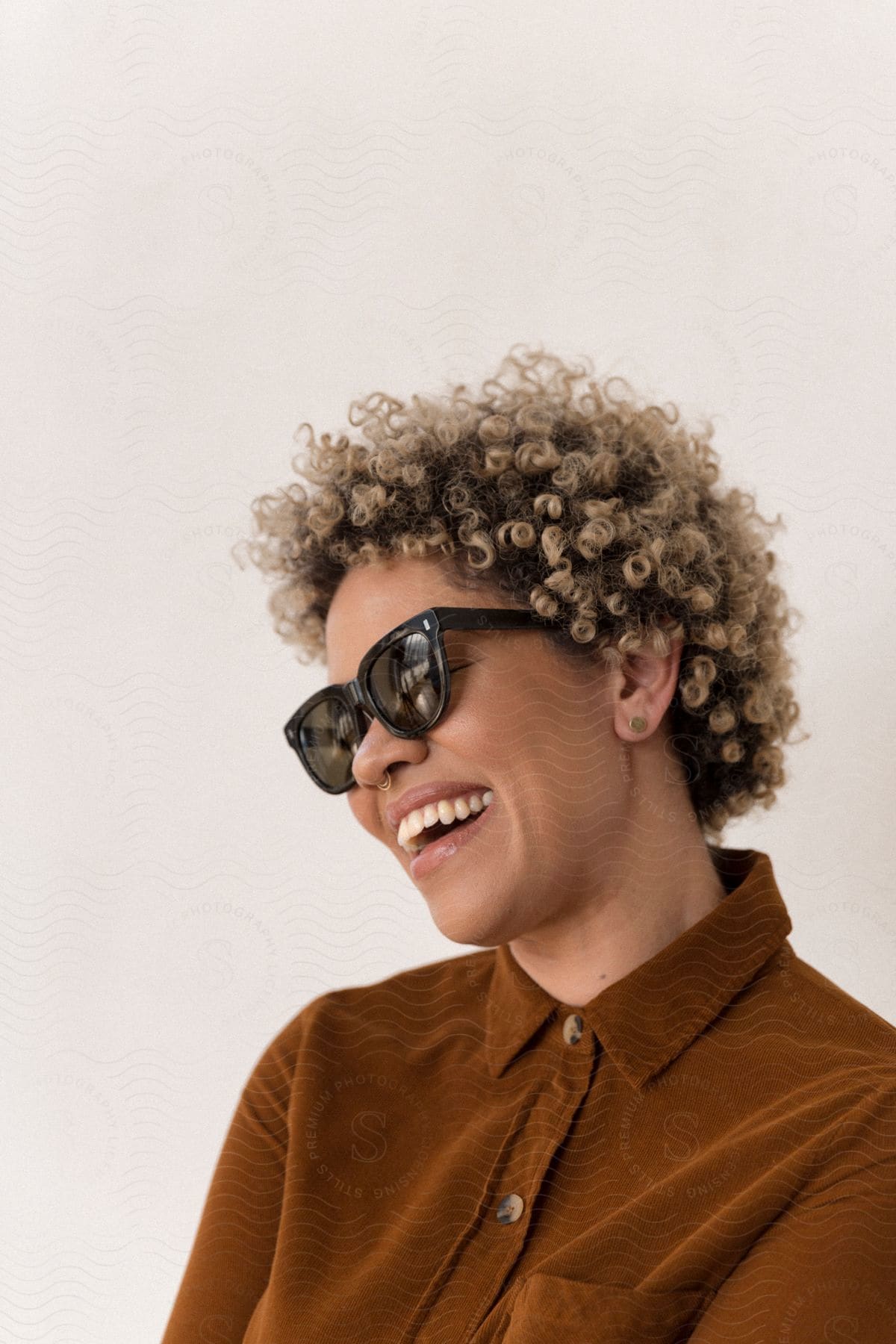 A portrait of a young women smiling while wearing sunglasses and a button-down shirt.