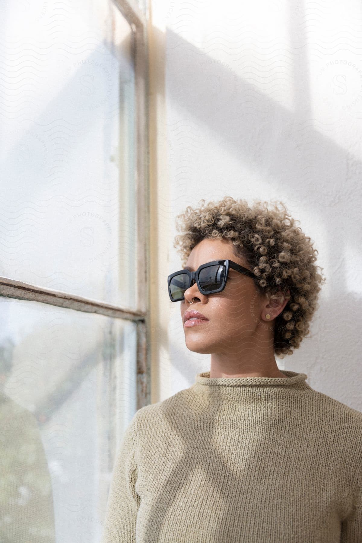 Black woman with curly hair who has a glasses on, looking left through a glass window in a room.