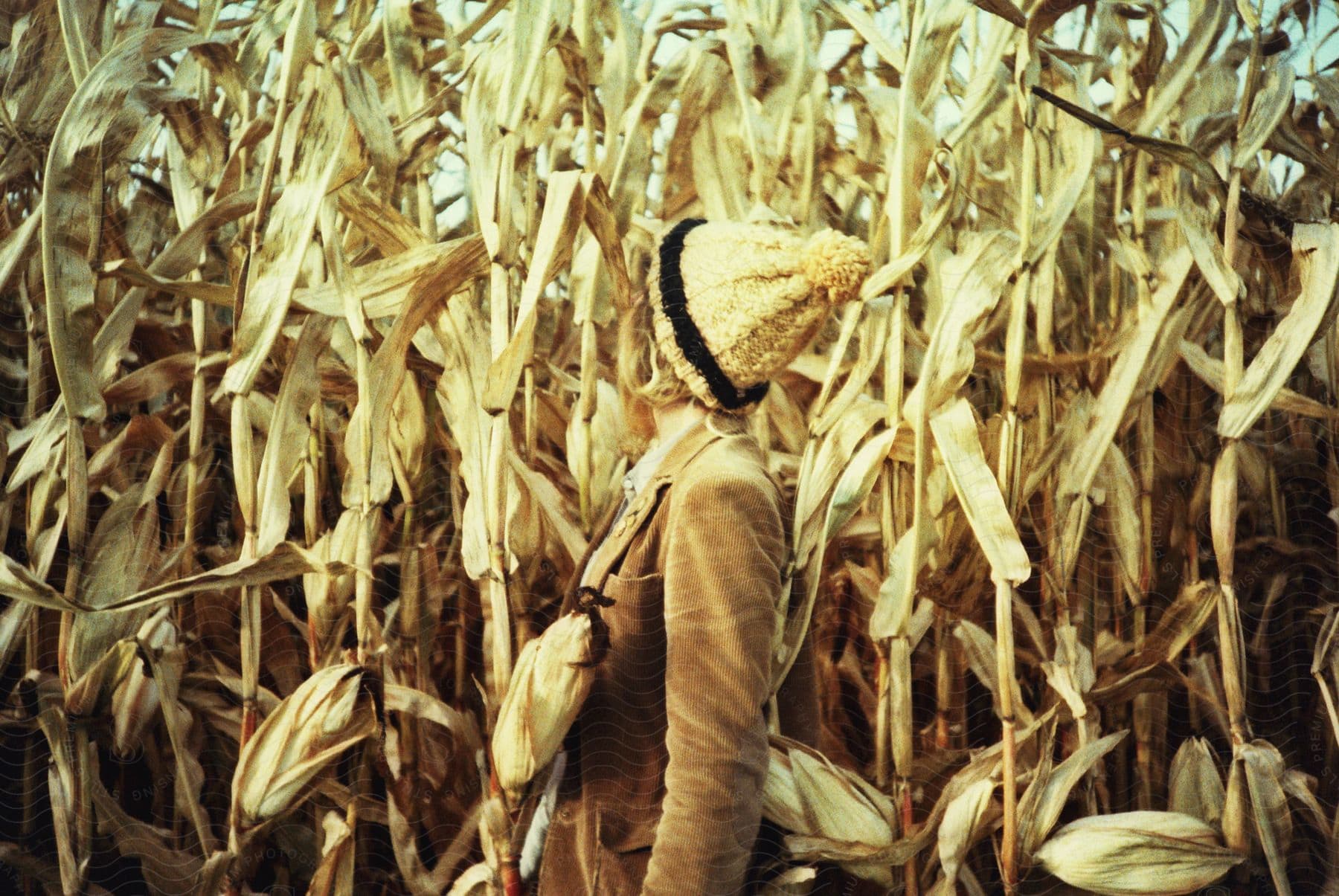 a woman turns to look at stalks of corn growing behind her