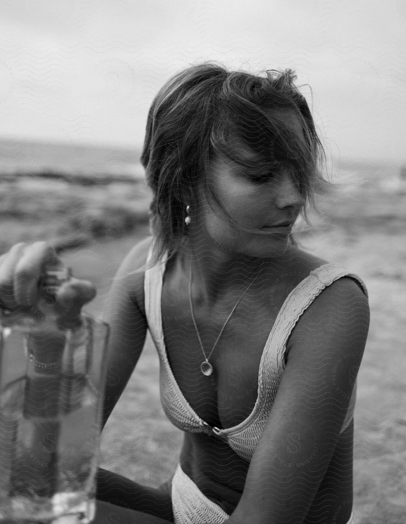 A woman holding a bottle of alcohol while sitting on the beach