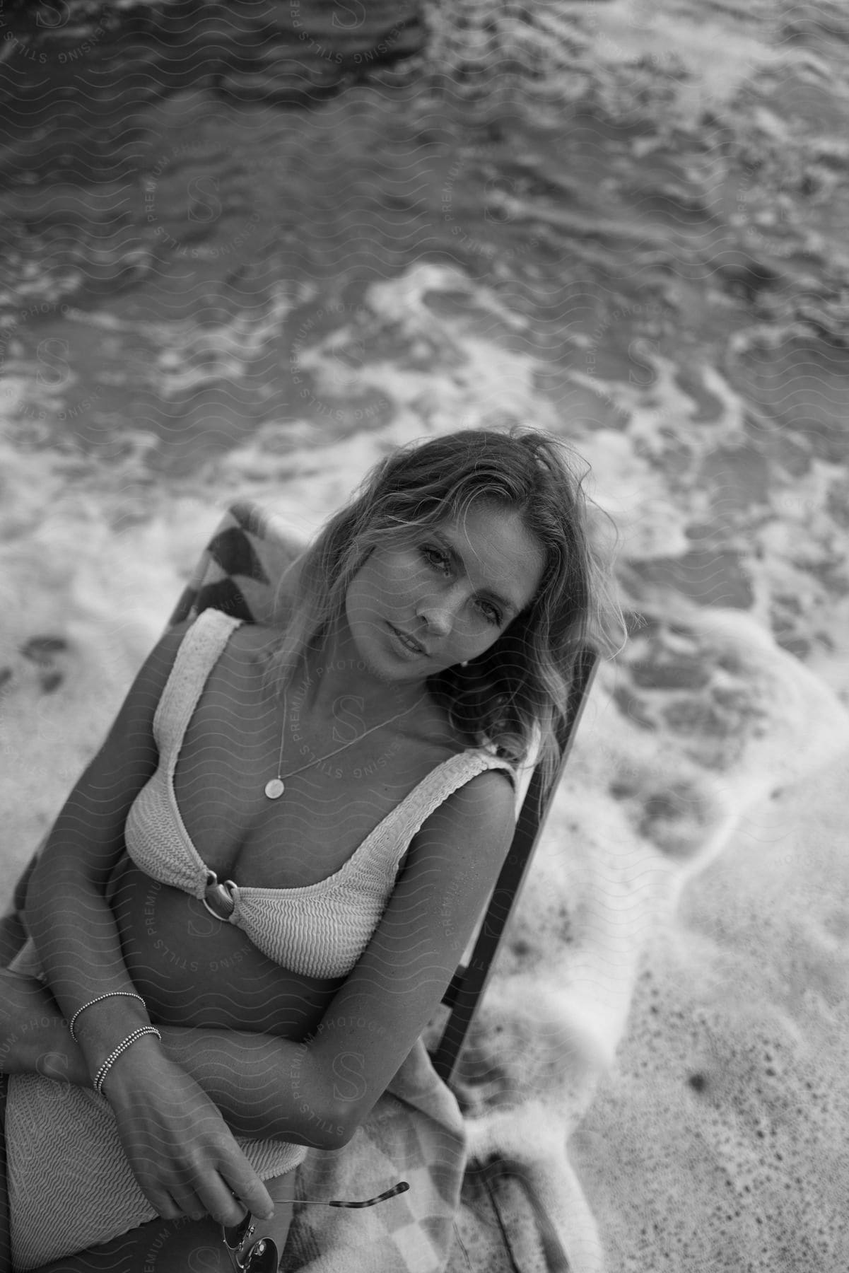 Woman with brown hair and white bikini sits in armchair on the beach