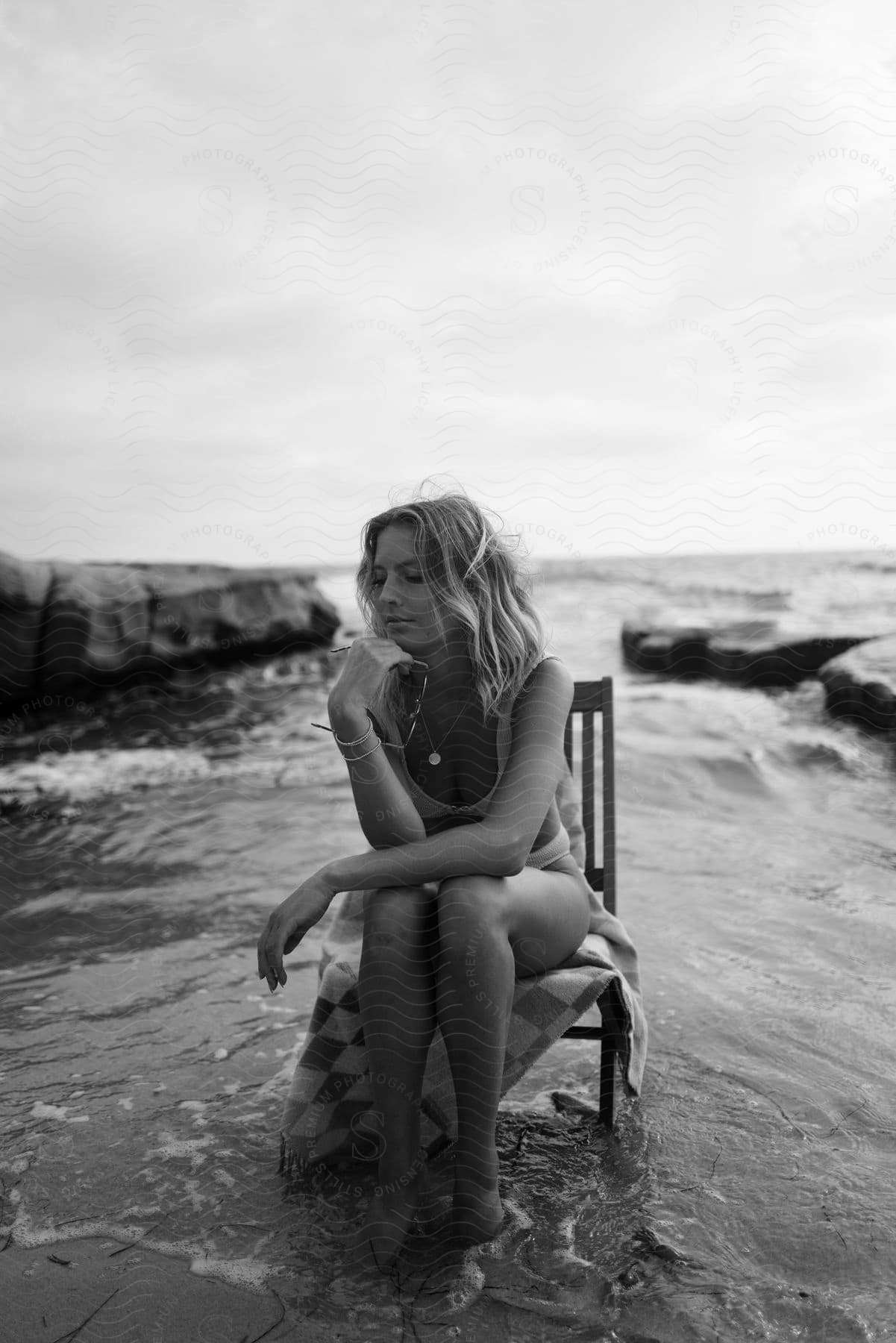 a woman sits on a wooden chair in the ocean along the coast