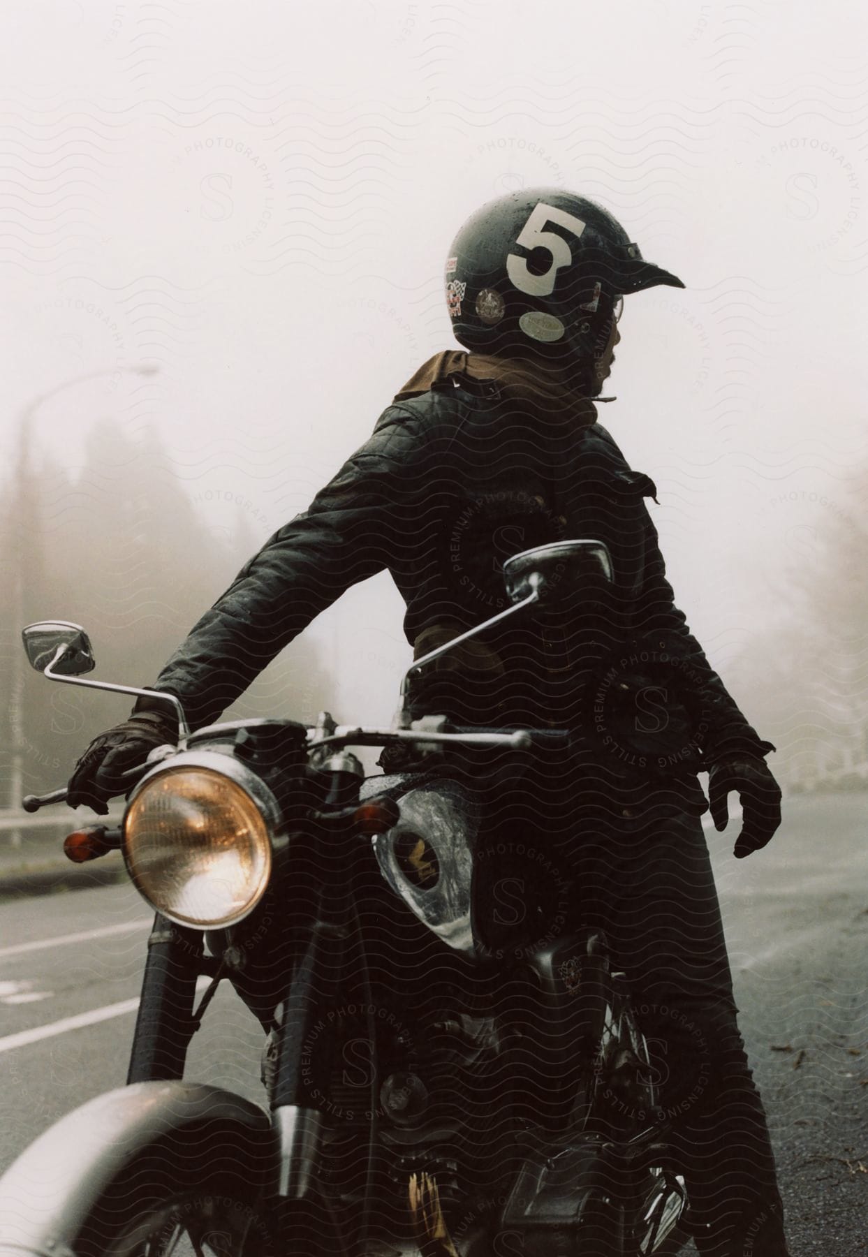 A man sitting on his motorcycle on the roadside looks at the fog covered road behind him