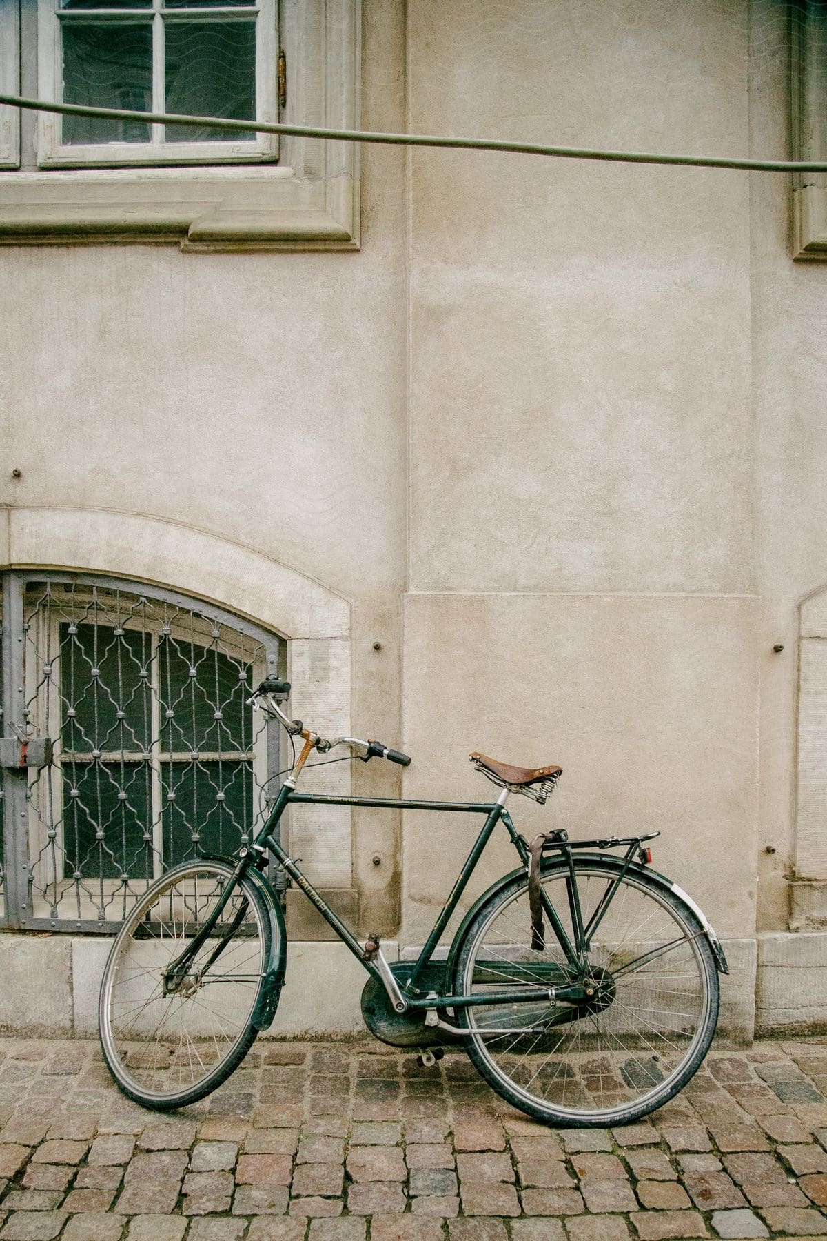 Bicycle leans against building wall on cobblestone path.