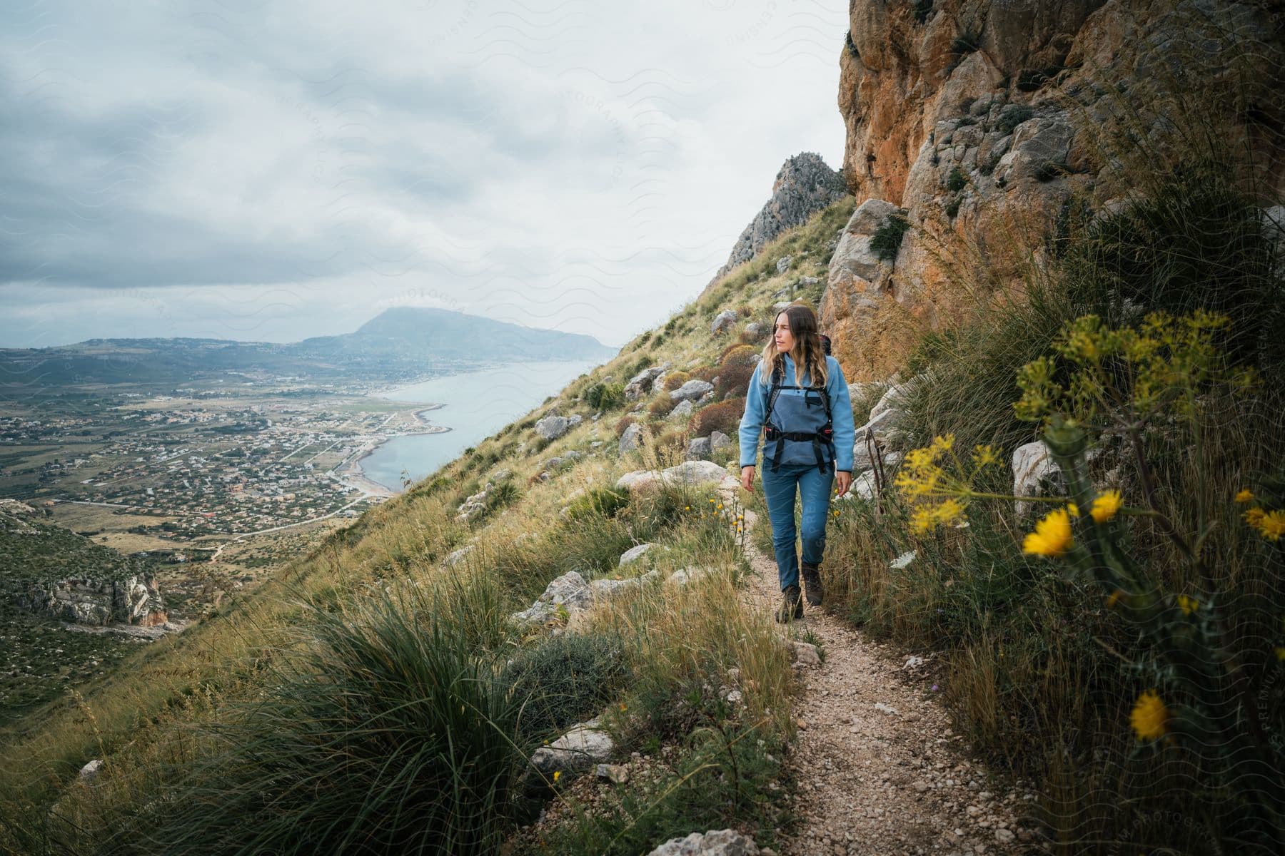 A woman with a backpack hiking on a narrow mountain path.