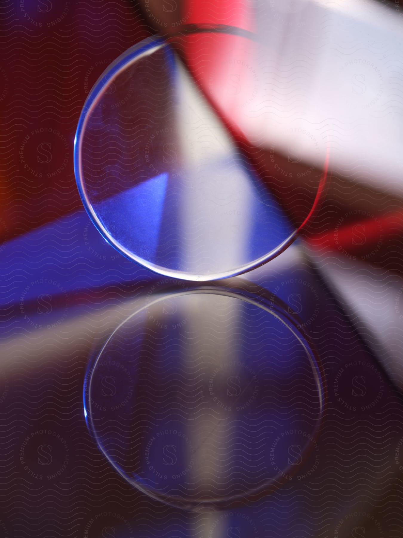 A clear, round object sits in front of red and blue angular shapes.