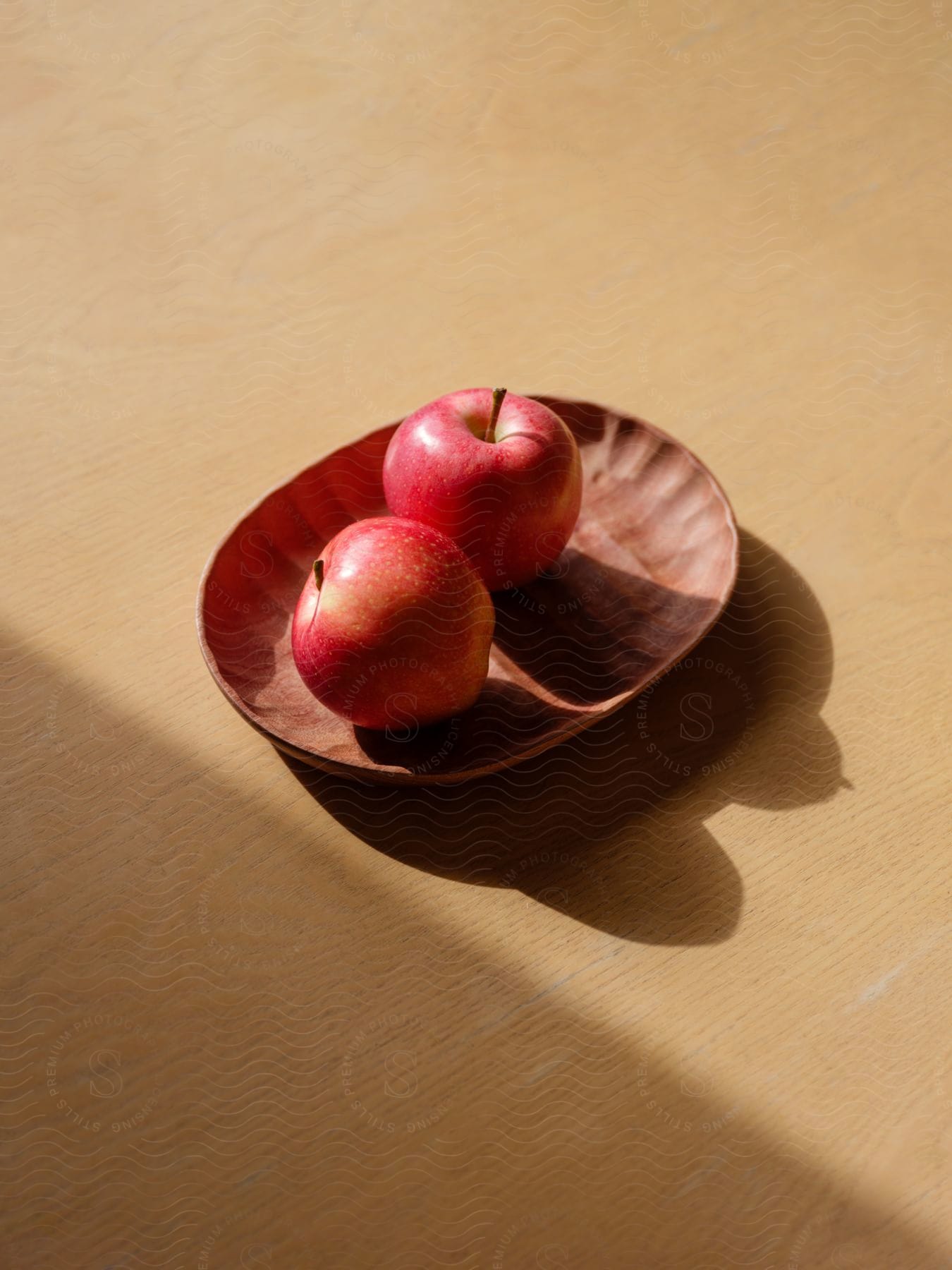 Two red apples on a brown plate