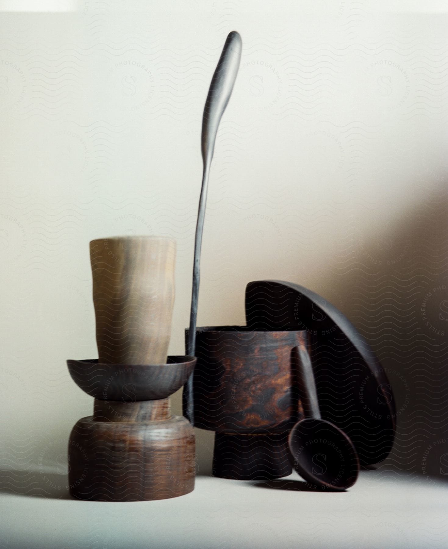 A pottery plate and spoon leans on a pottery cup while a wax candle stands on another pottery cup.