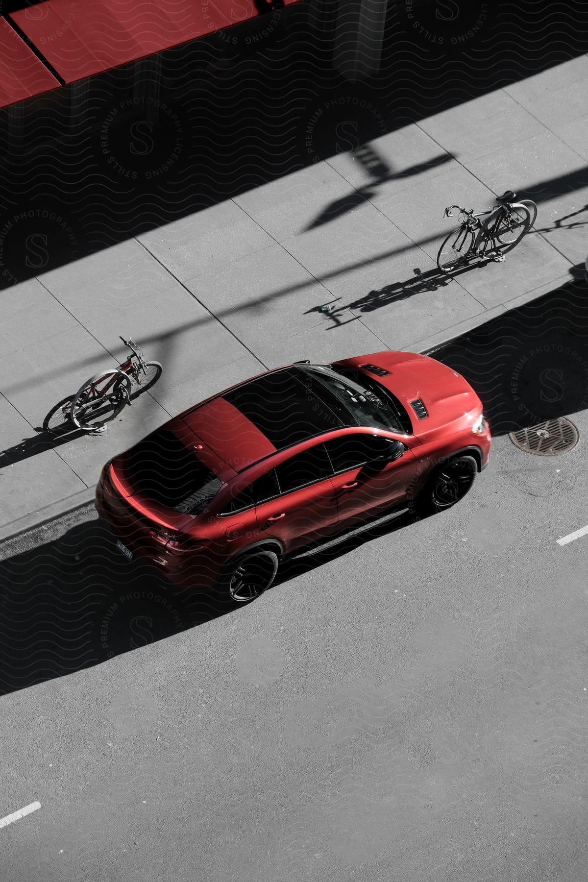 A red automobile is parked along side a city street near some locked bicycles.