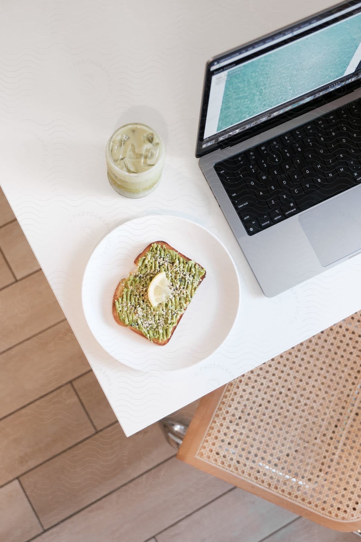 an avocado toast on a plate next to a smoothie beside a laptop on a table