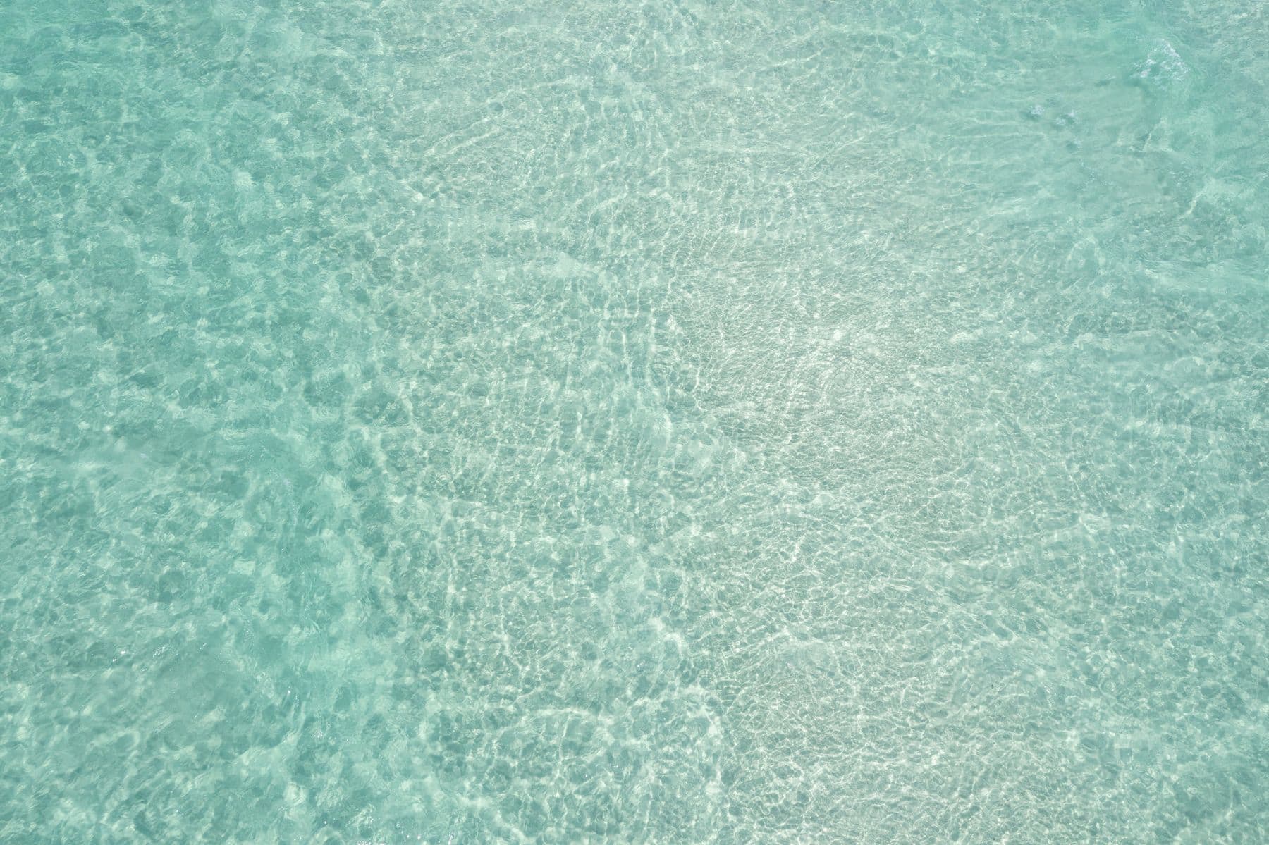 An aerial view of a sparkling blue sea and glistening white sand, bathed in the sunlight.