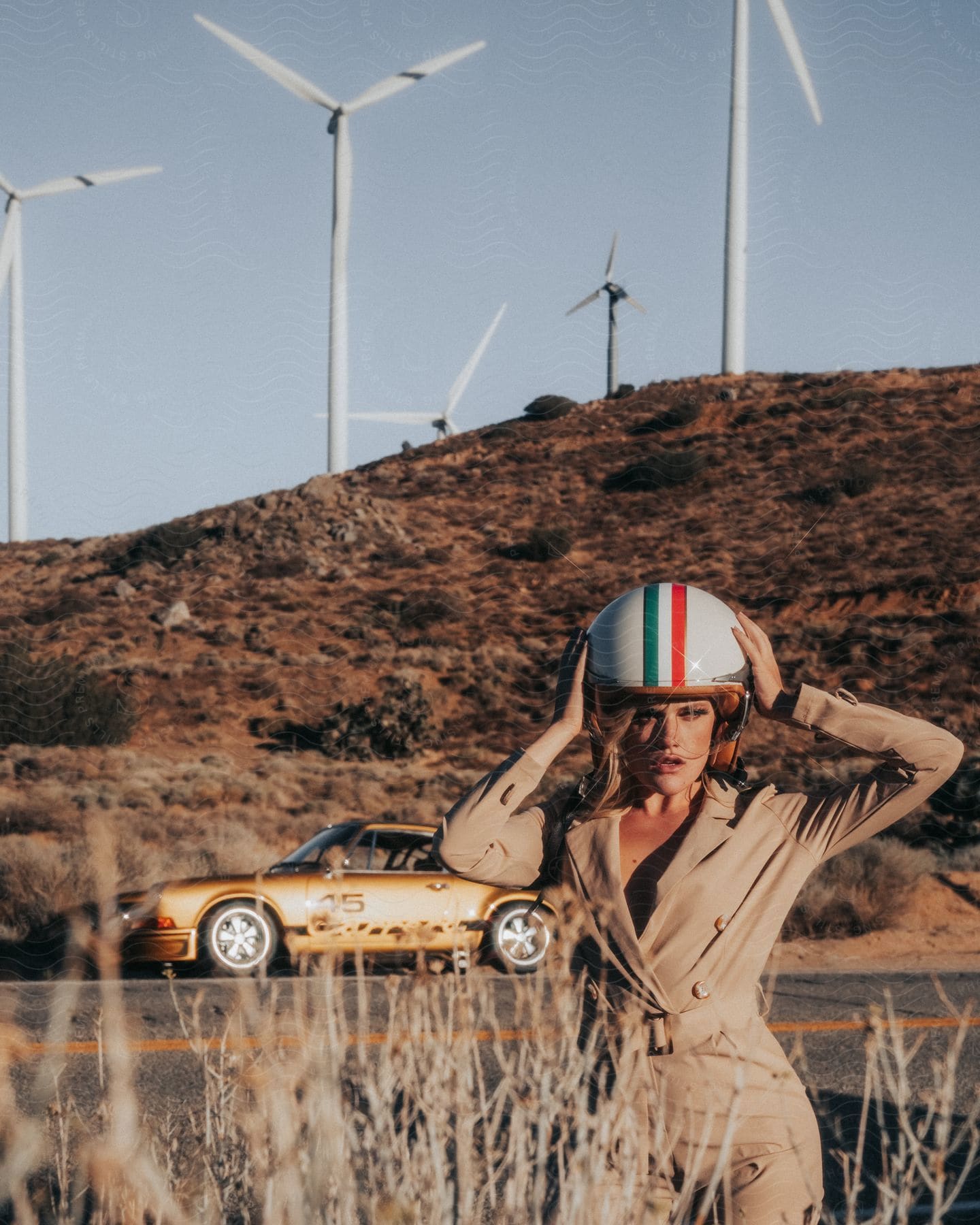 A woman wearing a helmet and racing outfit posing in front of a car