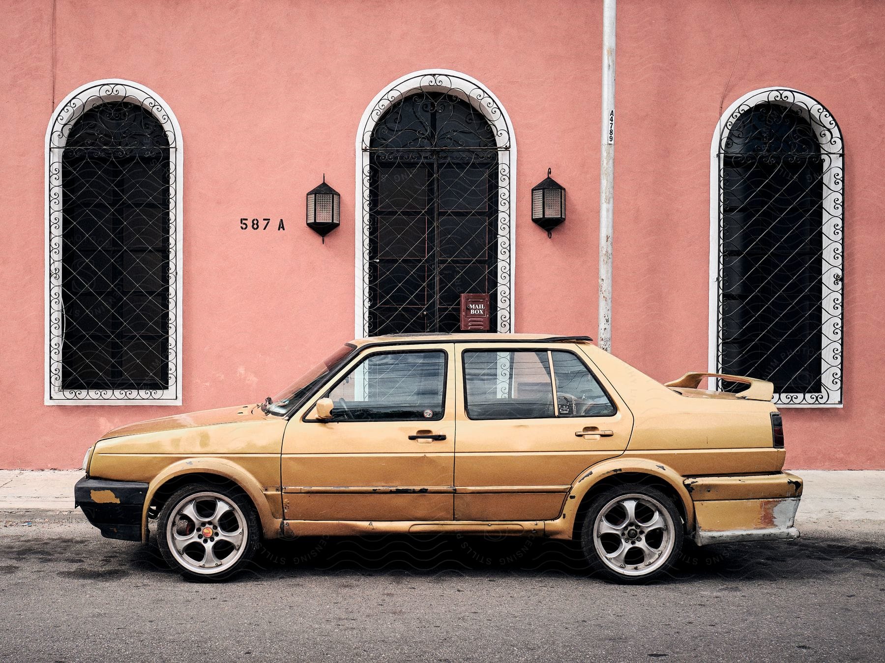 Beat up gold car parked in front of a coral colored wall with arched windows