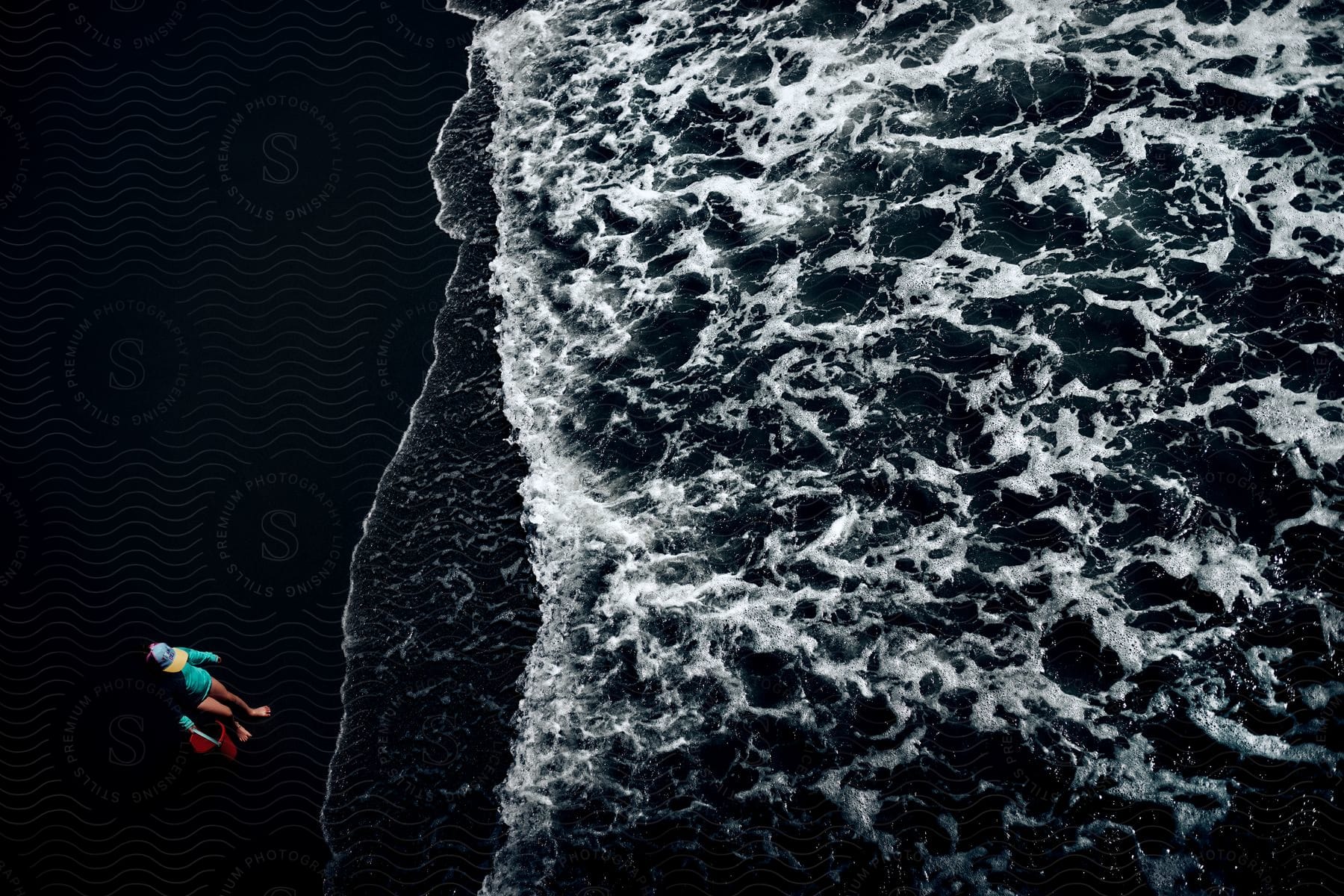 Aerial Of A Woman Sitting In A Chair On A Dark Beach As Waves Crash In The Ocean In Front Of Her