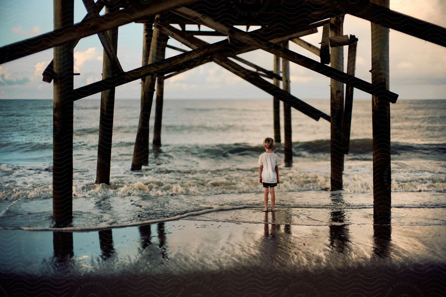 A Young Child Standing Under A Pier At The Beach Looking Out Into The Ocean