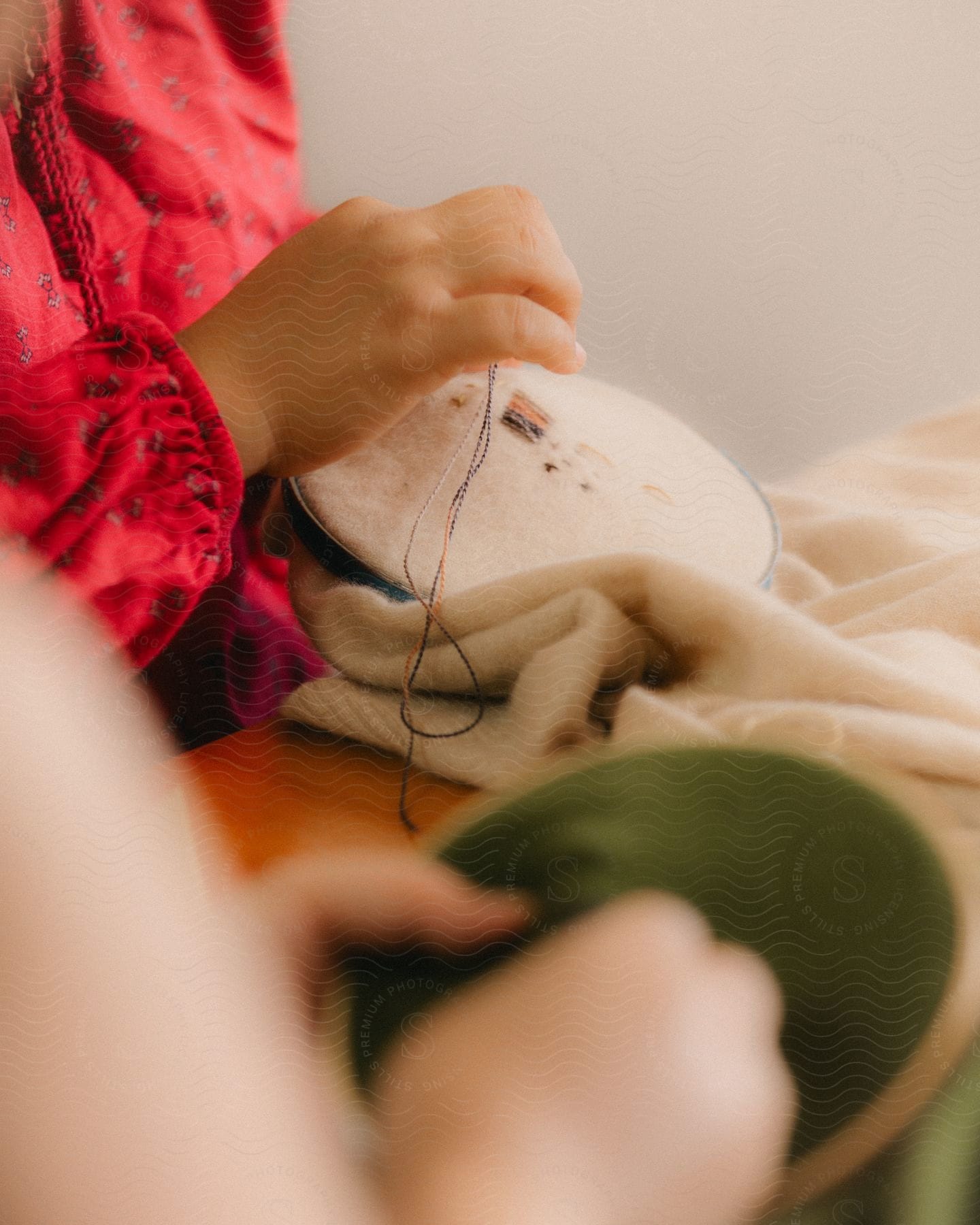 Two people weaving threads on fabric indoors.