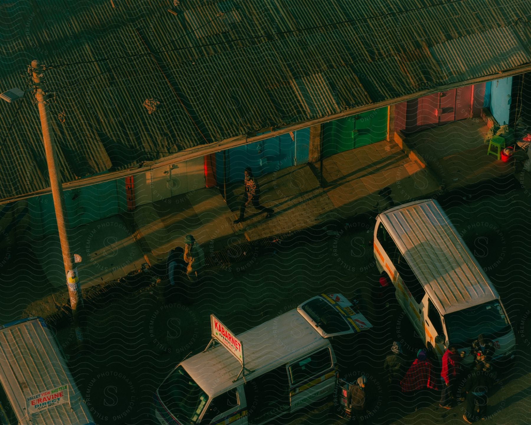 A pair of vans used to taxi people in Kenya are parked and people are standing nearby.