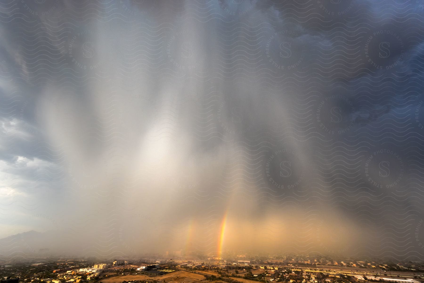 An aerial view of a rainbow emerging from a rain cloud over a city