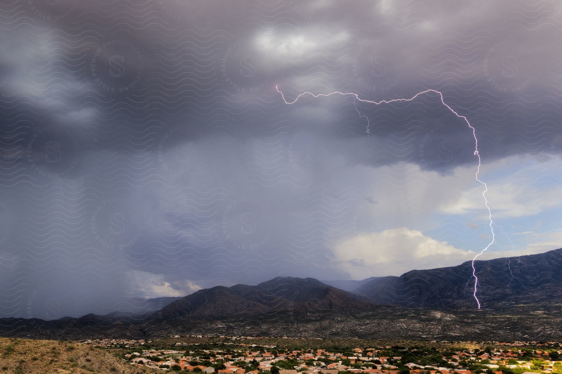 a lightning bolt is seen over a city striking near a mountain range being rained on