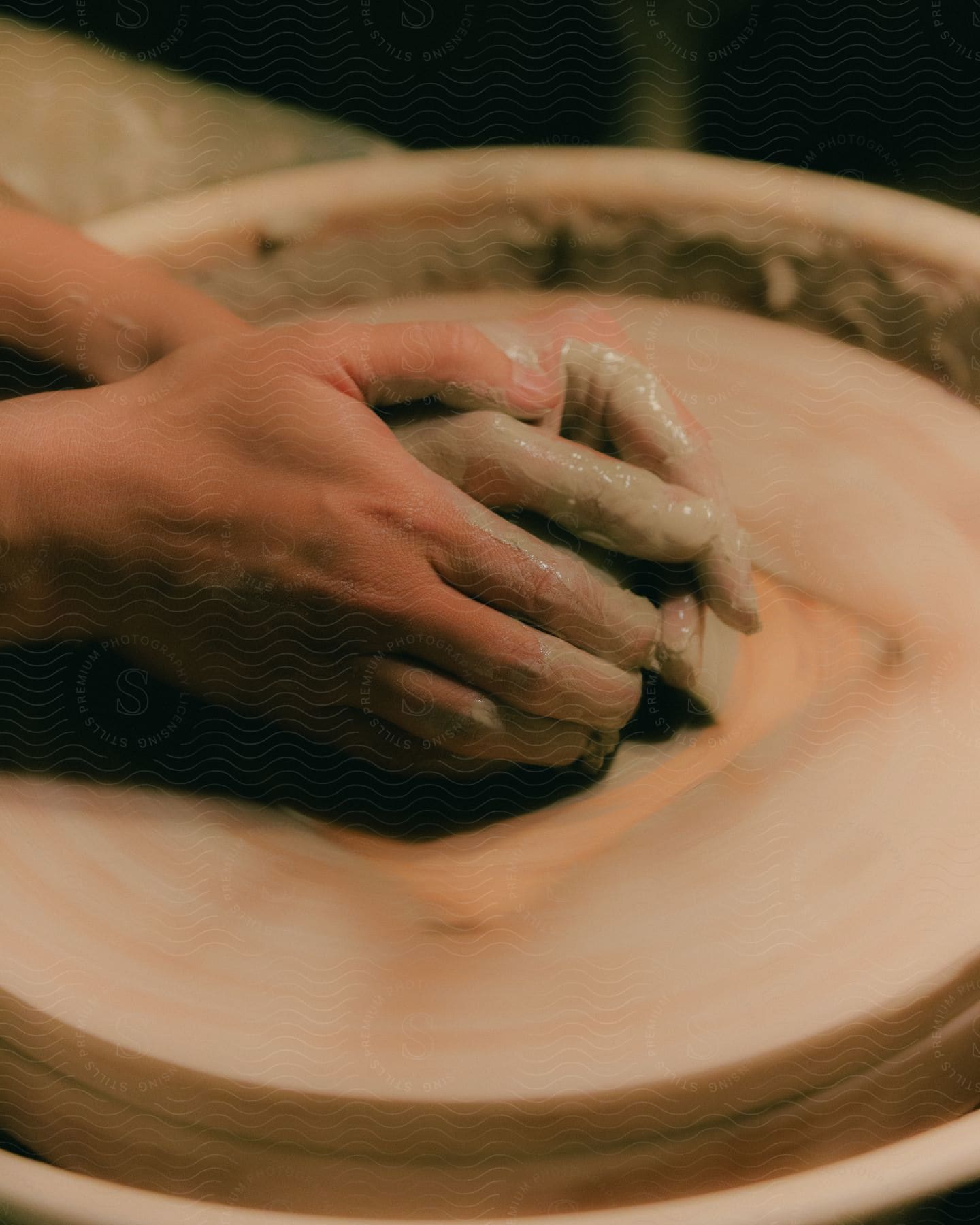 A woman is working with wet clay in her hands on a pottery wheel