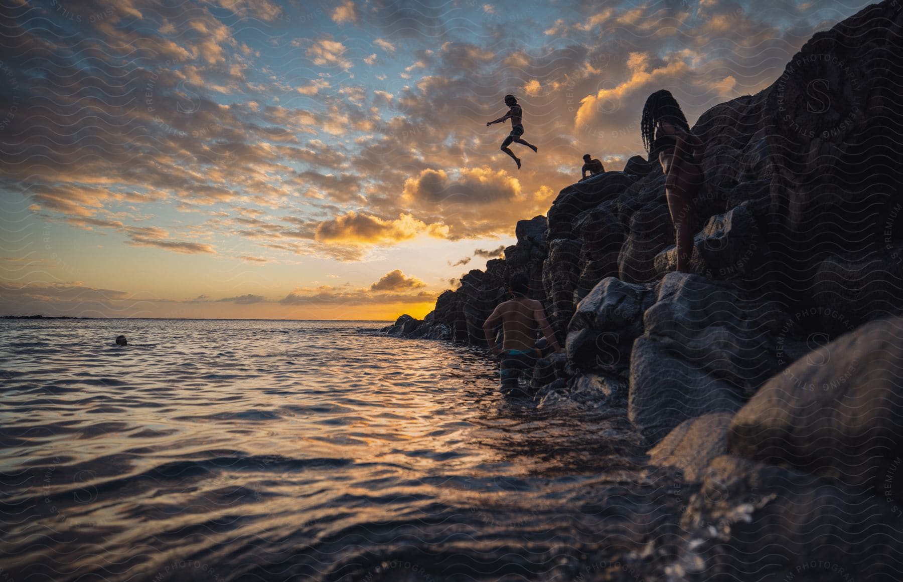 A man jumps off a cliff into the water while friends look on.