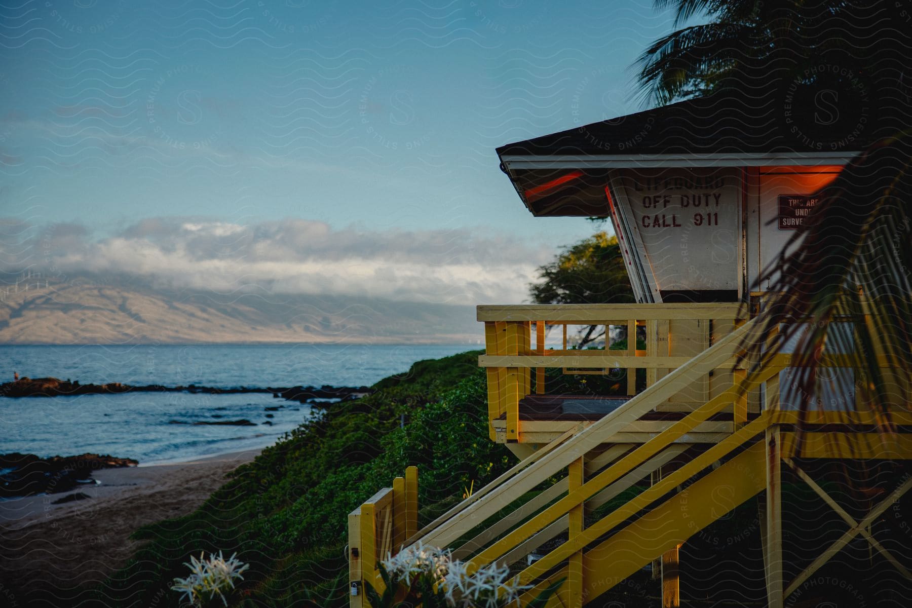 Tower with a balcony and stairs overlooking the beach near a hill covered with plants and vegetation