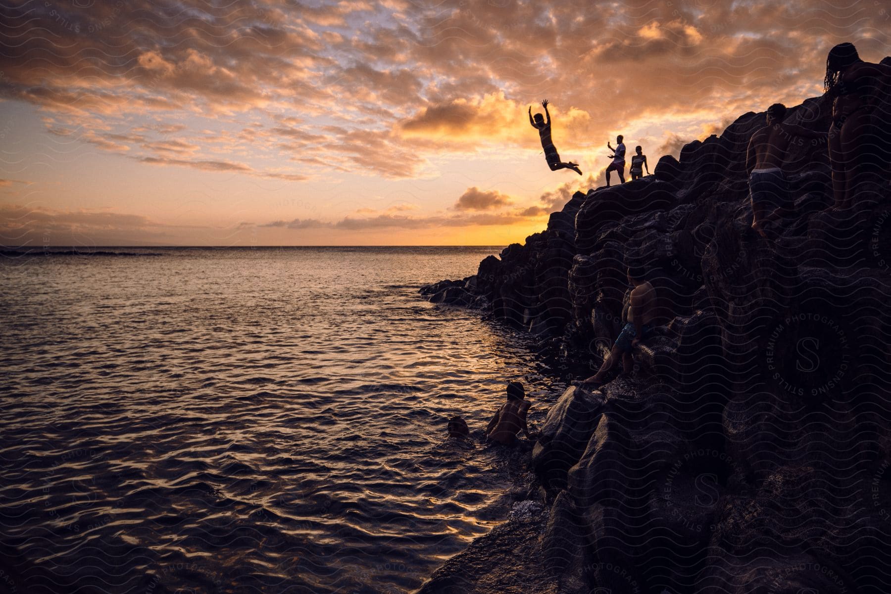 Group of people have fun on the coast of a beach next to the ocean at sunset