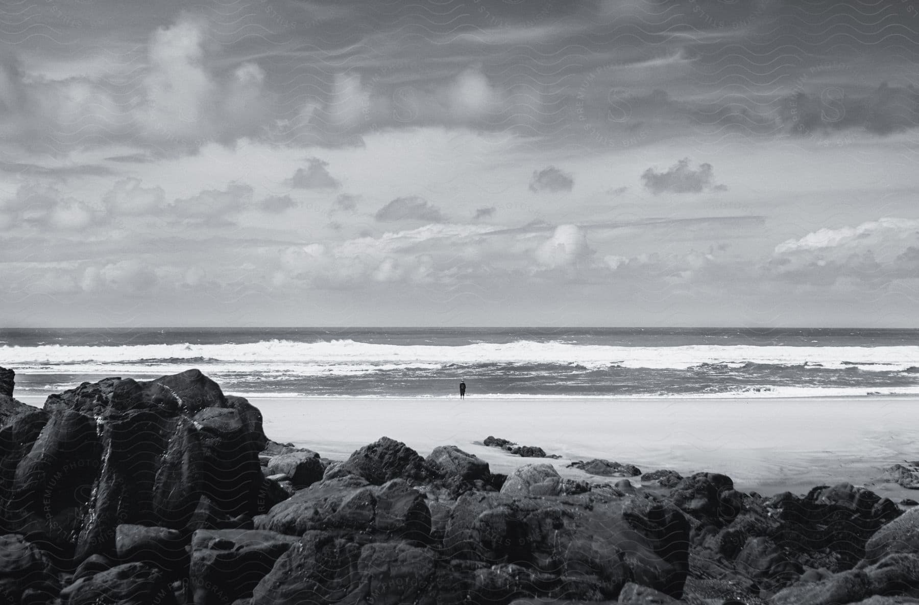 Distant man stands on the beach in front of the rocks near the ocean