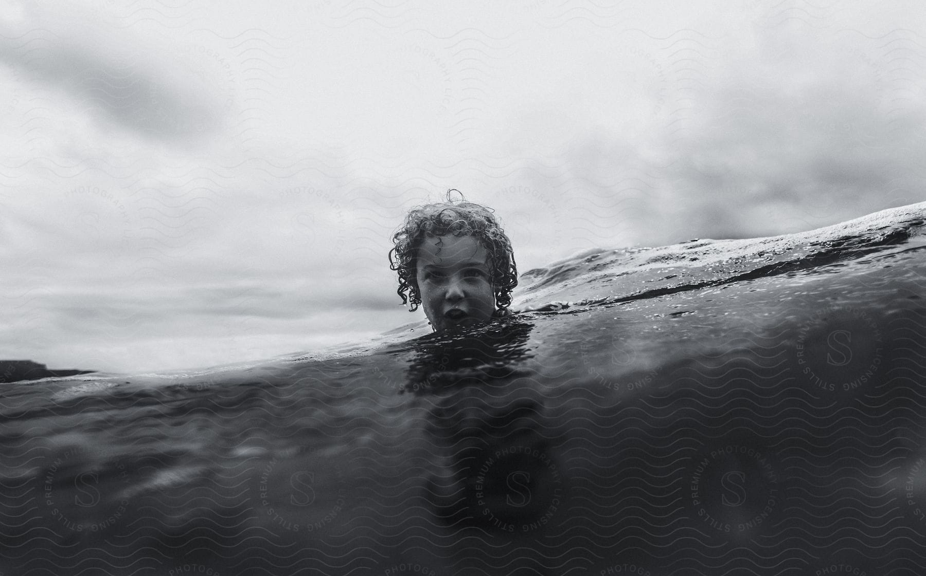 Water of swelling wave covers chin of girl on overcast day.