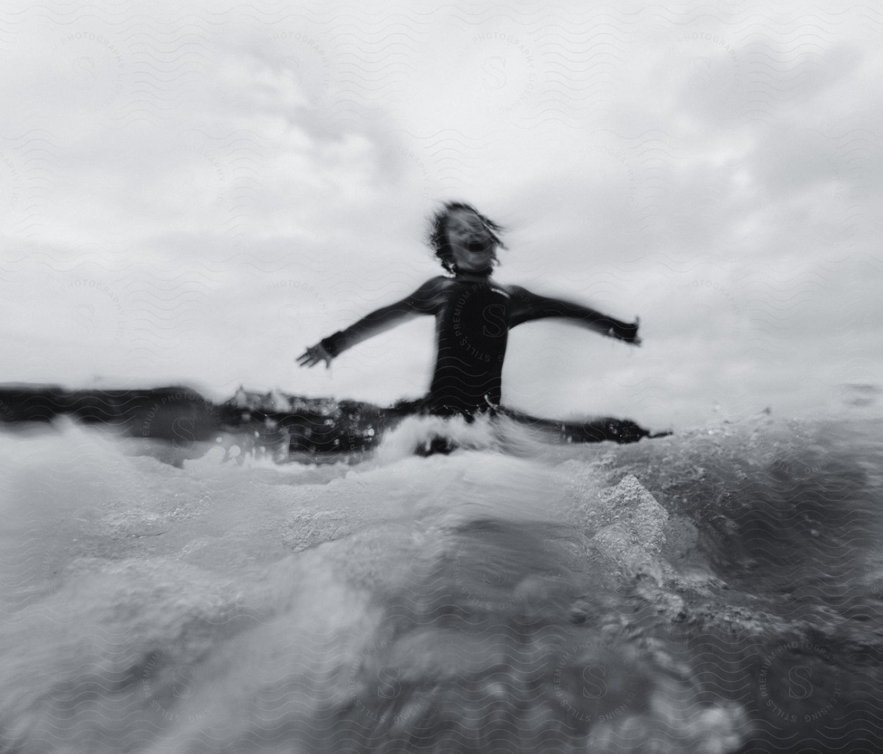 A boy sitting on a surfboard catching a wave while raising his arms.